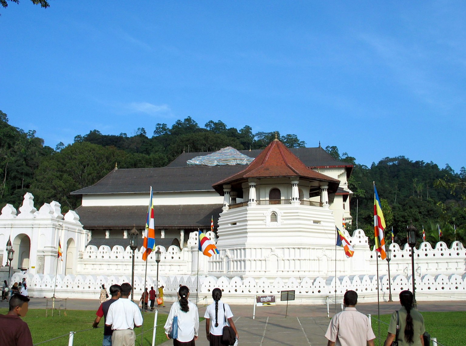 Exterior of a white temple with flags and lush greenery