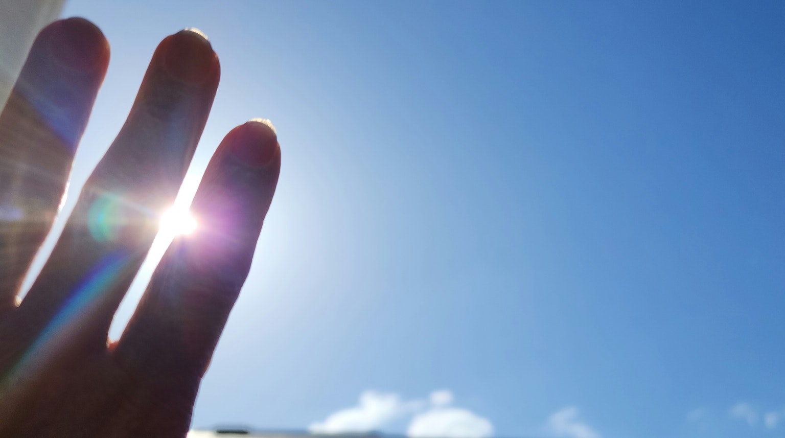 Mano alcanzando el brillante sol contra un cielo azul