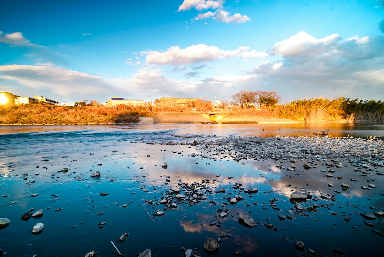 Ruhige Wasseroberfläche, die den blauen Himmel und Wolken mit verstreuten Steinen reflektiert