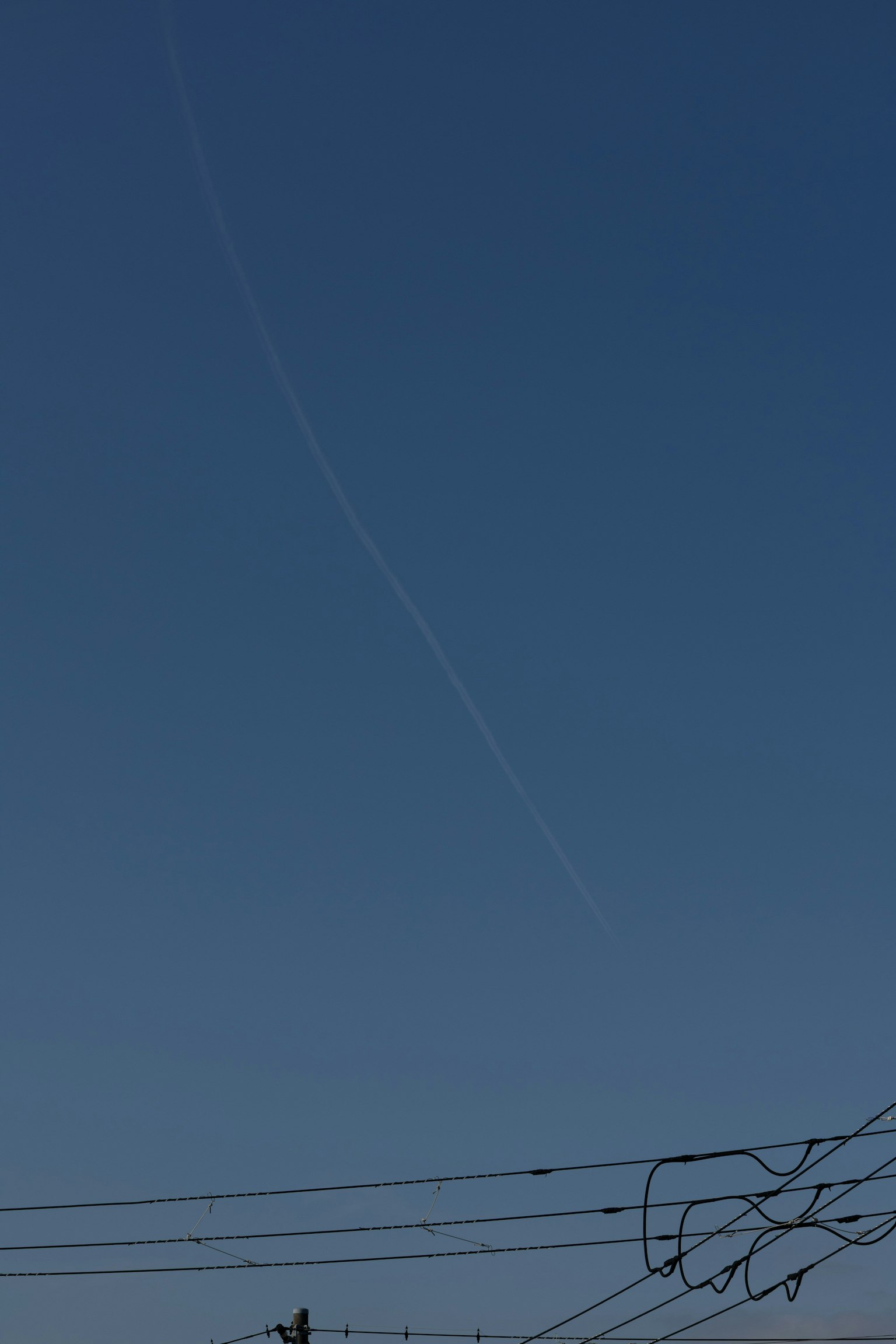 青空に飛行機雲が見える風景 電線が前景にある