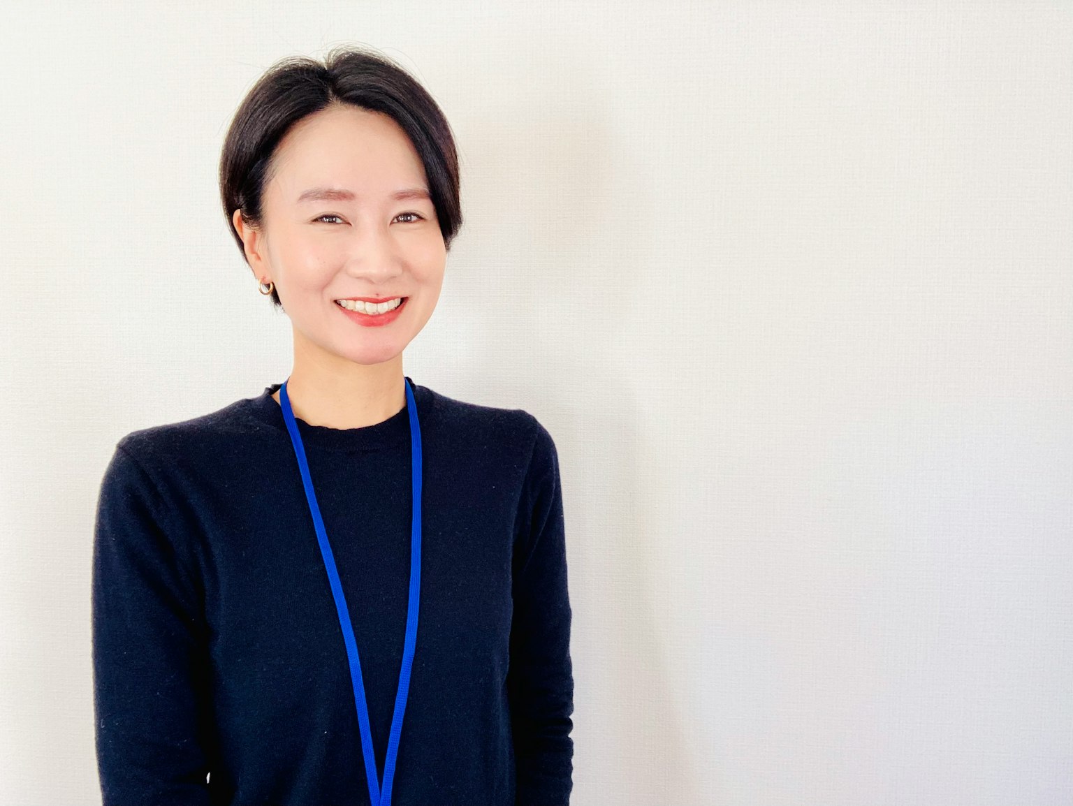 微笑的女性穿着黑色毛衣和蓝色项链站在白色墙壁前