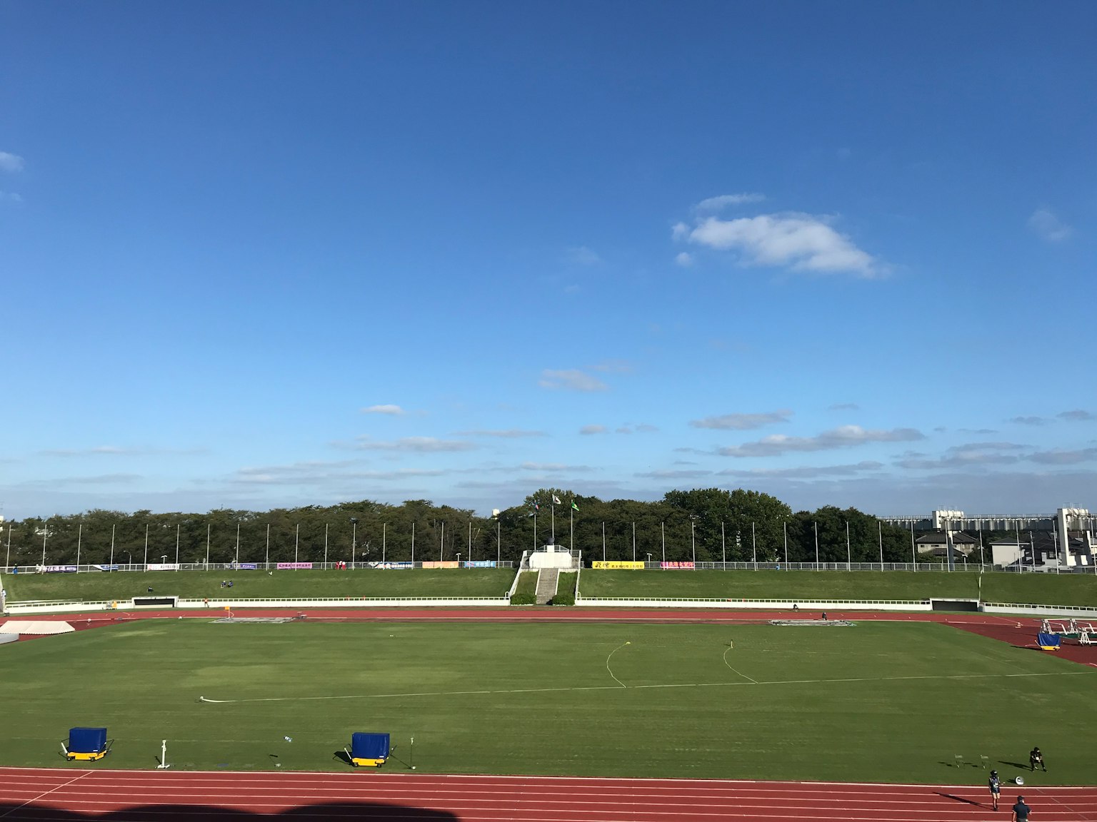 A panoramic view of a sports field with a clear blue sky and green grass