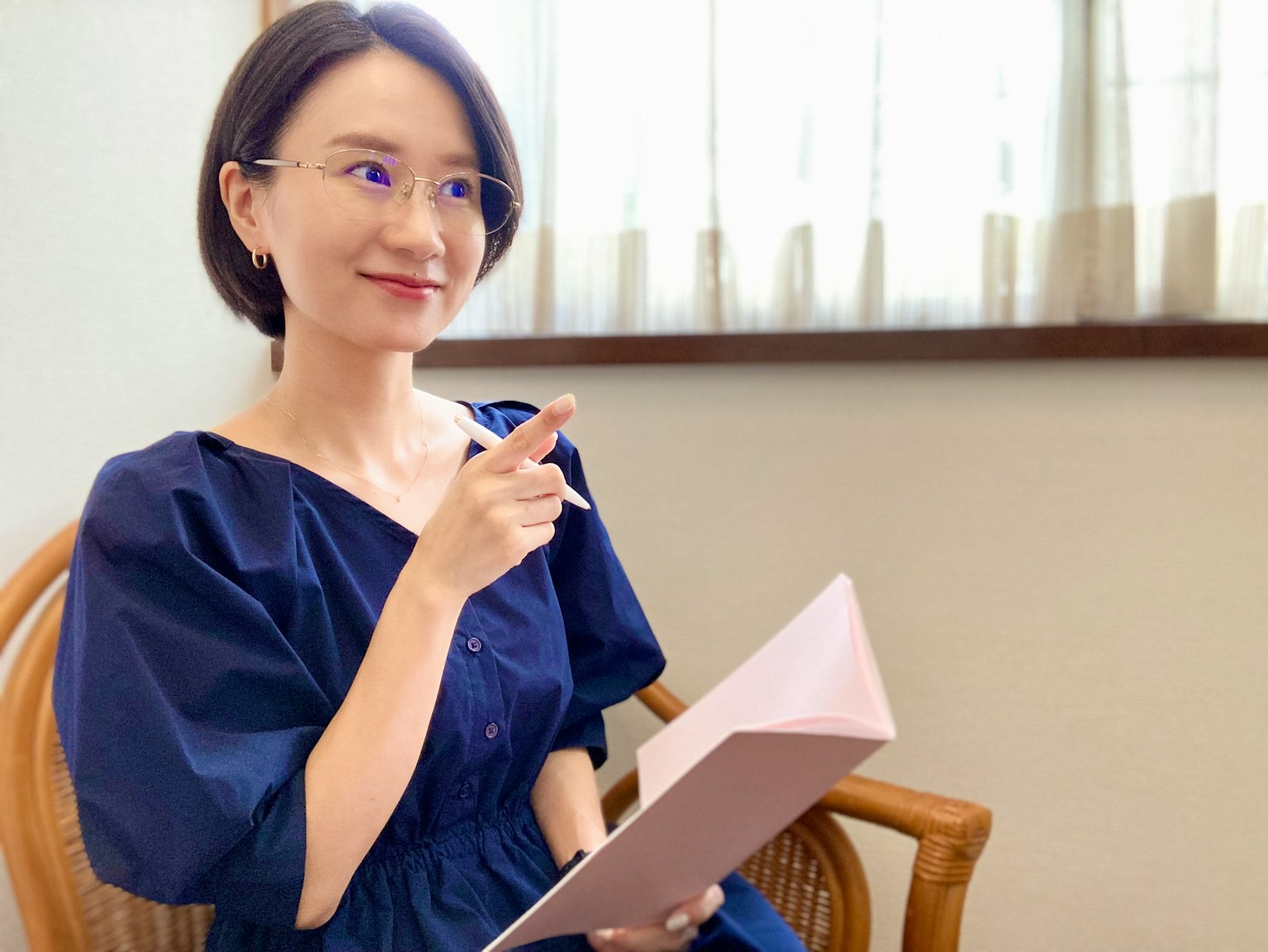 Mujer con vestido azul sosteniendo un cuaderno y señalando mientras sonríe