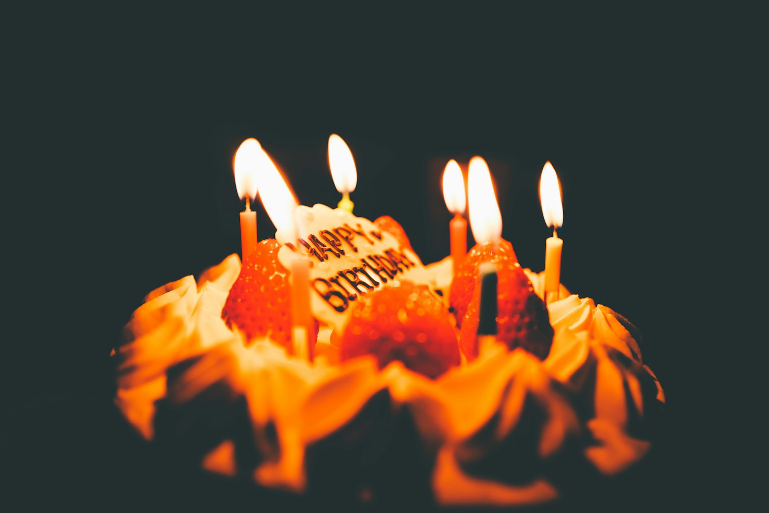 Pastel de cumpleaños con velas encendidas y decoraciones de fresas