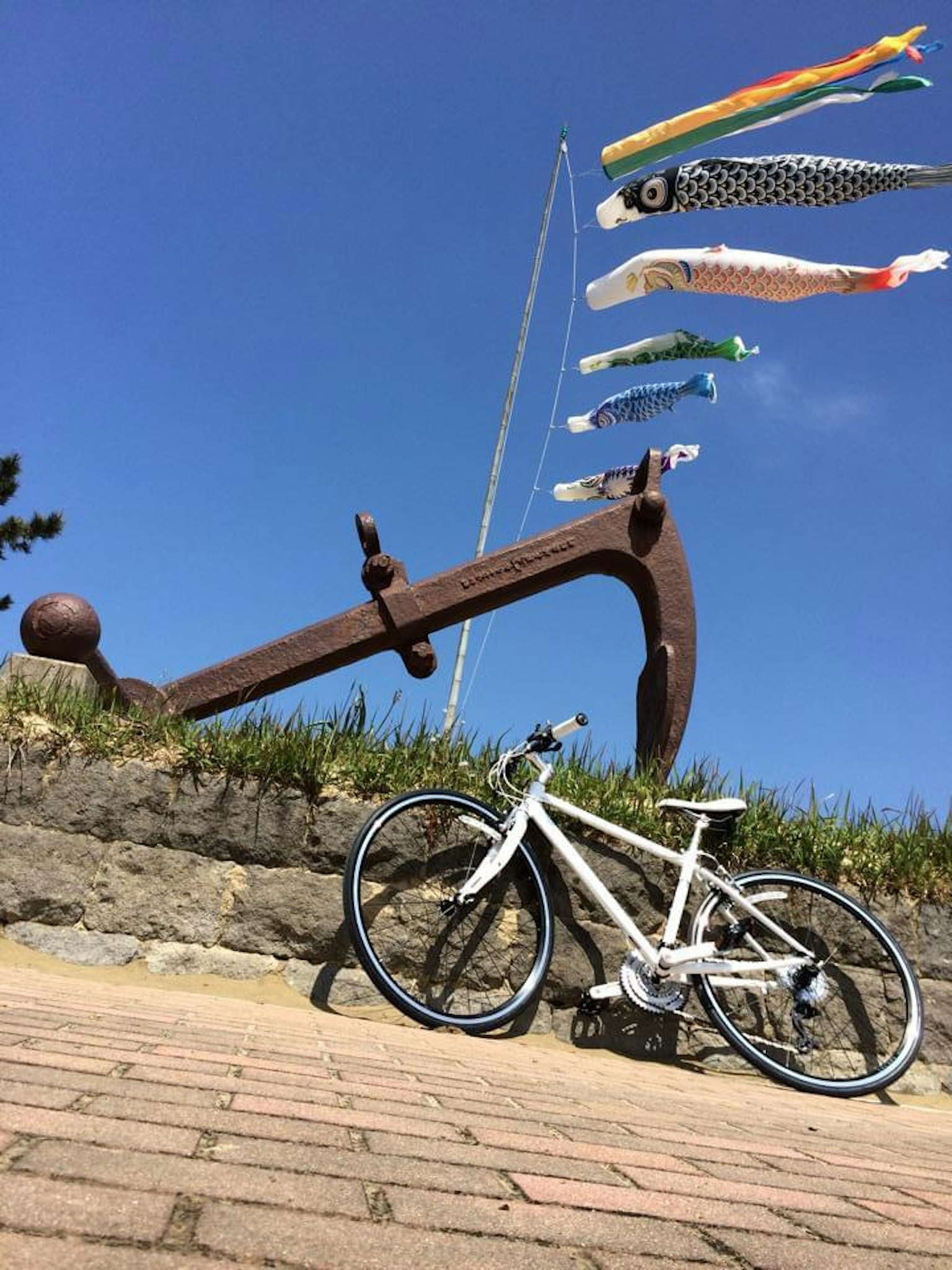 Una bicicleta blanca junto a un gran ancla de hierro bajo un cielo azul