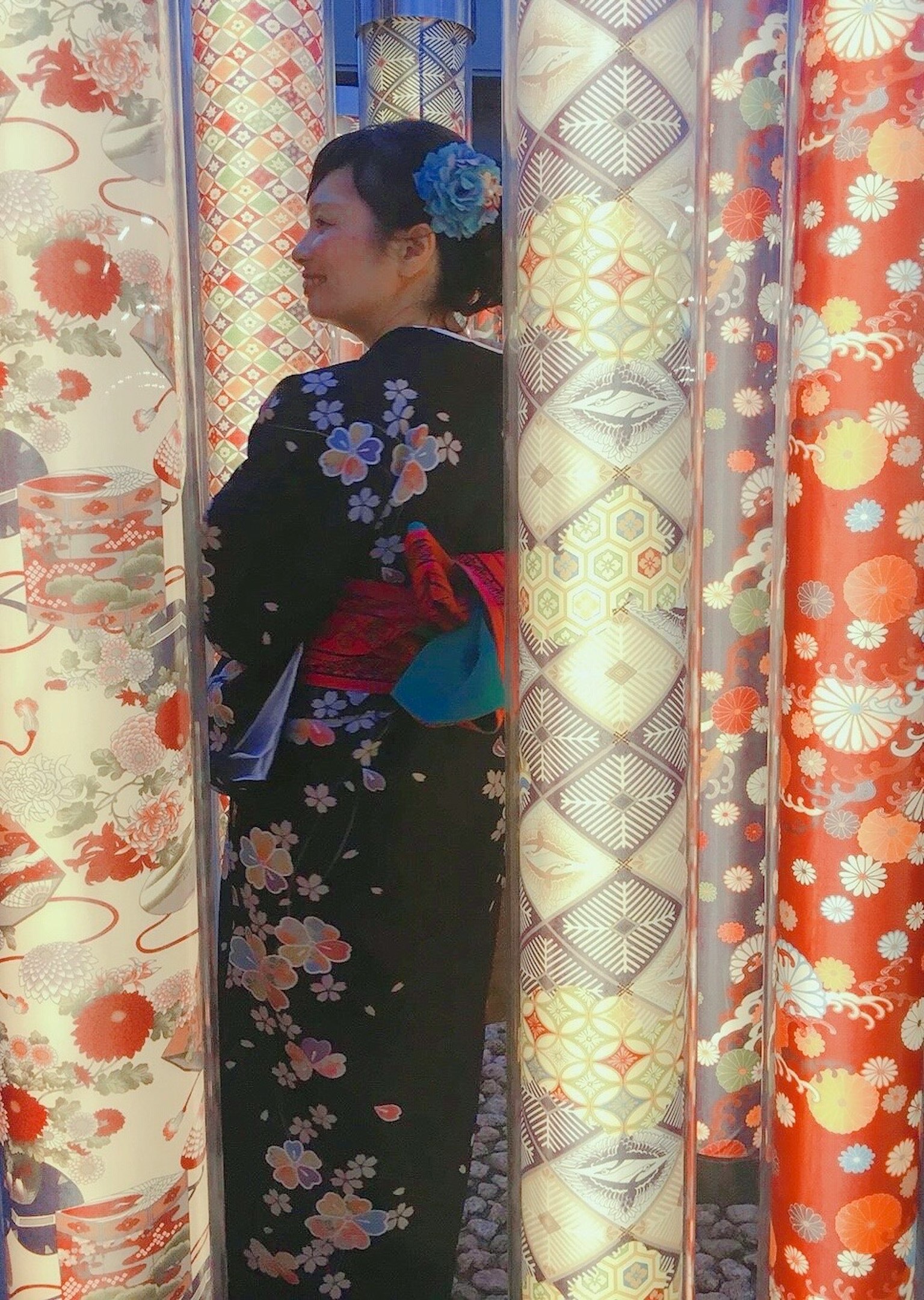 Một người phụ nữ trong trang phục kimono đứng giữa những cột nhiều màu sắc