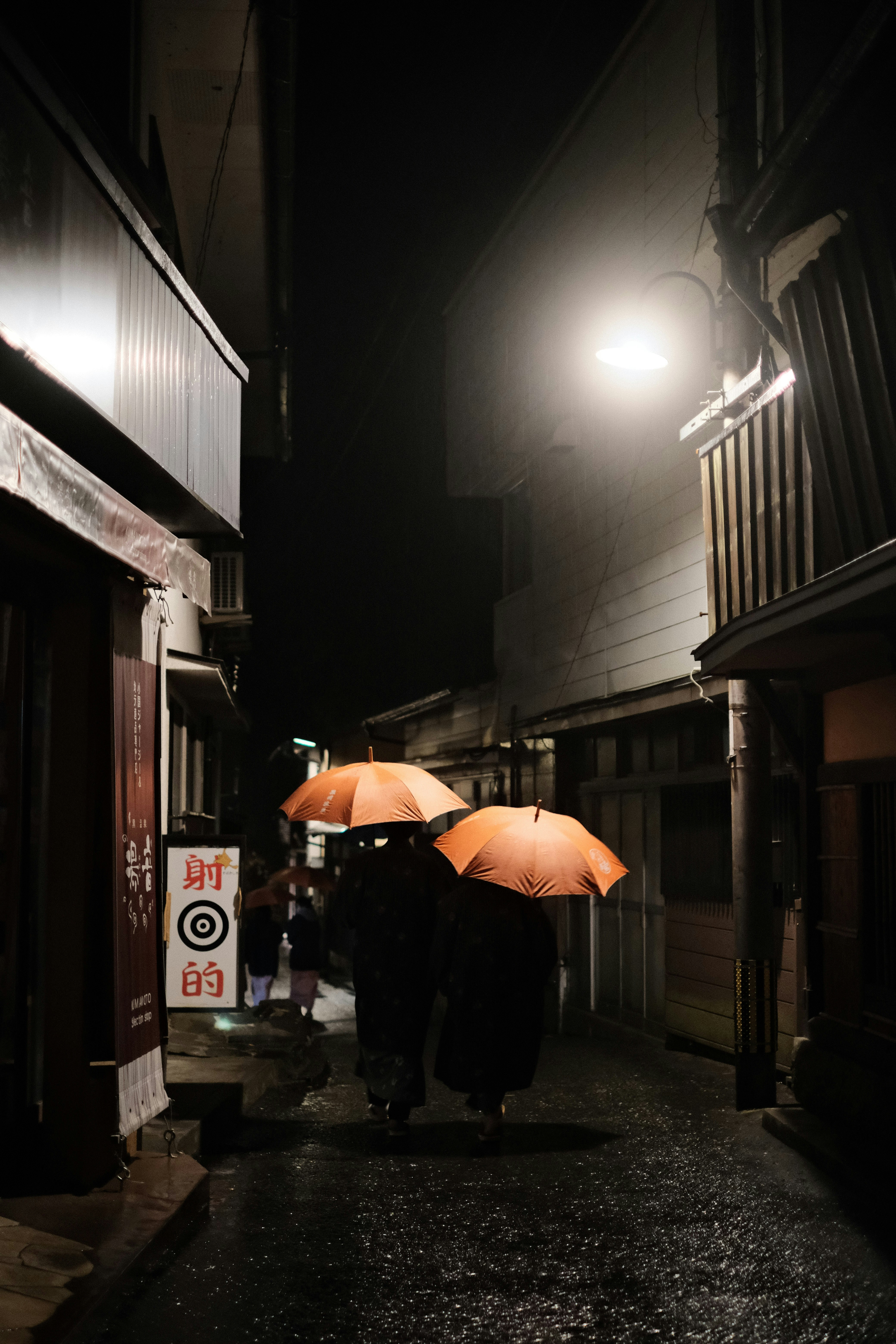 夜の街並みを歩く二人の人物がオレンジ色の傘を持っている