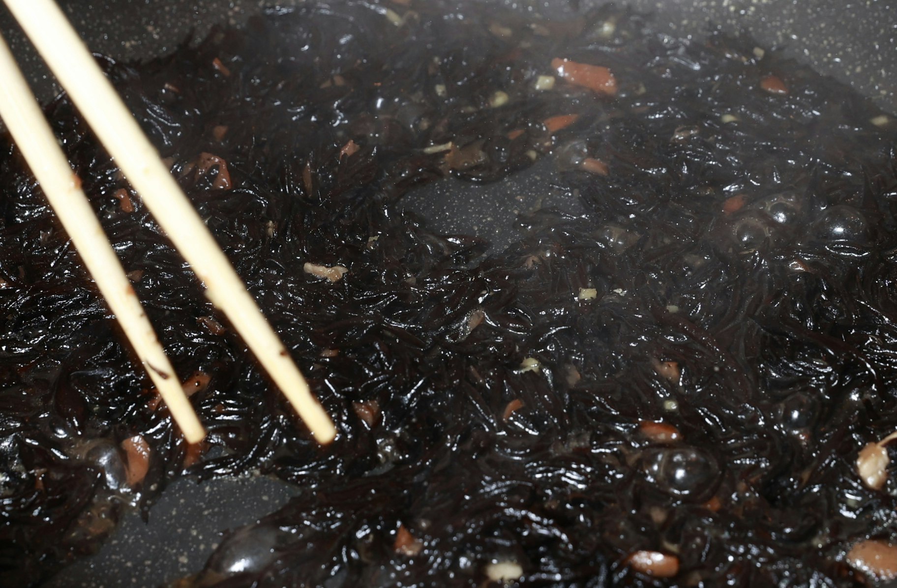 mengaduk sup hitam di dalam panci dengan sumpit
