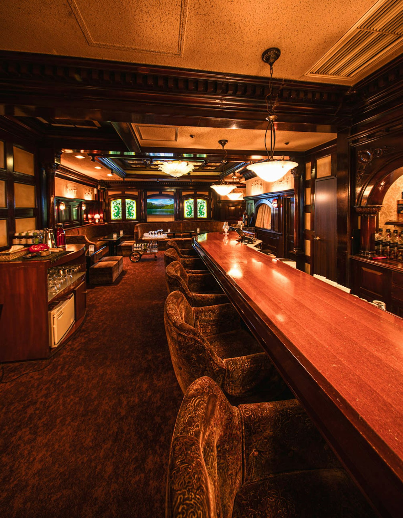 Interior de bar acogedor con un largo mostrador de madera y asientos cómodos bajo una suave iluminación