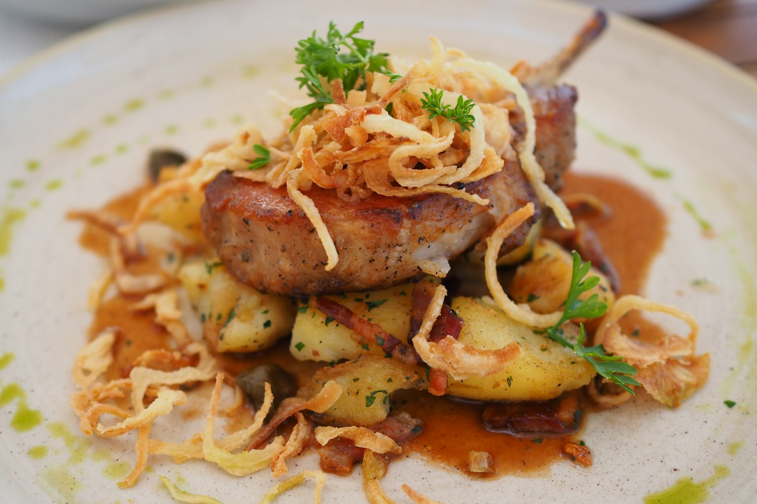 Un plat de viande joliment présenté avec des pommes de terre, garni de persil et d'oignons frits croustillants