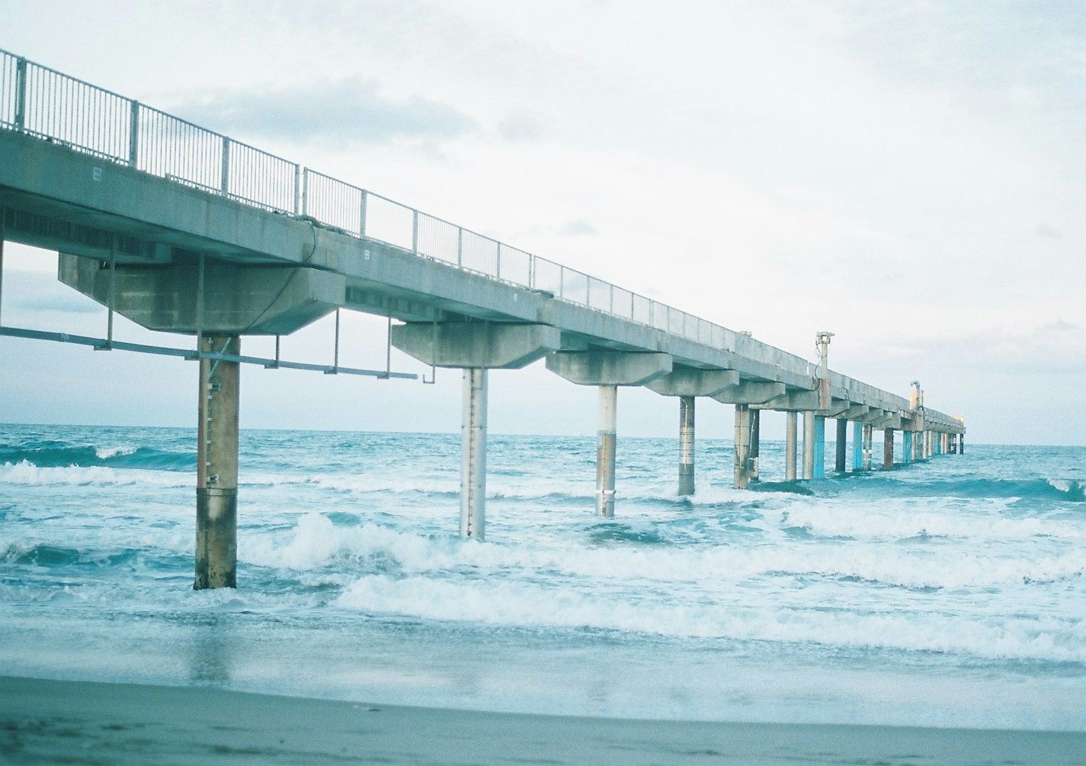 Vista escénica de un muelle que se extiende hacia el mar con olas rompiendo