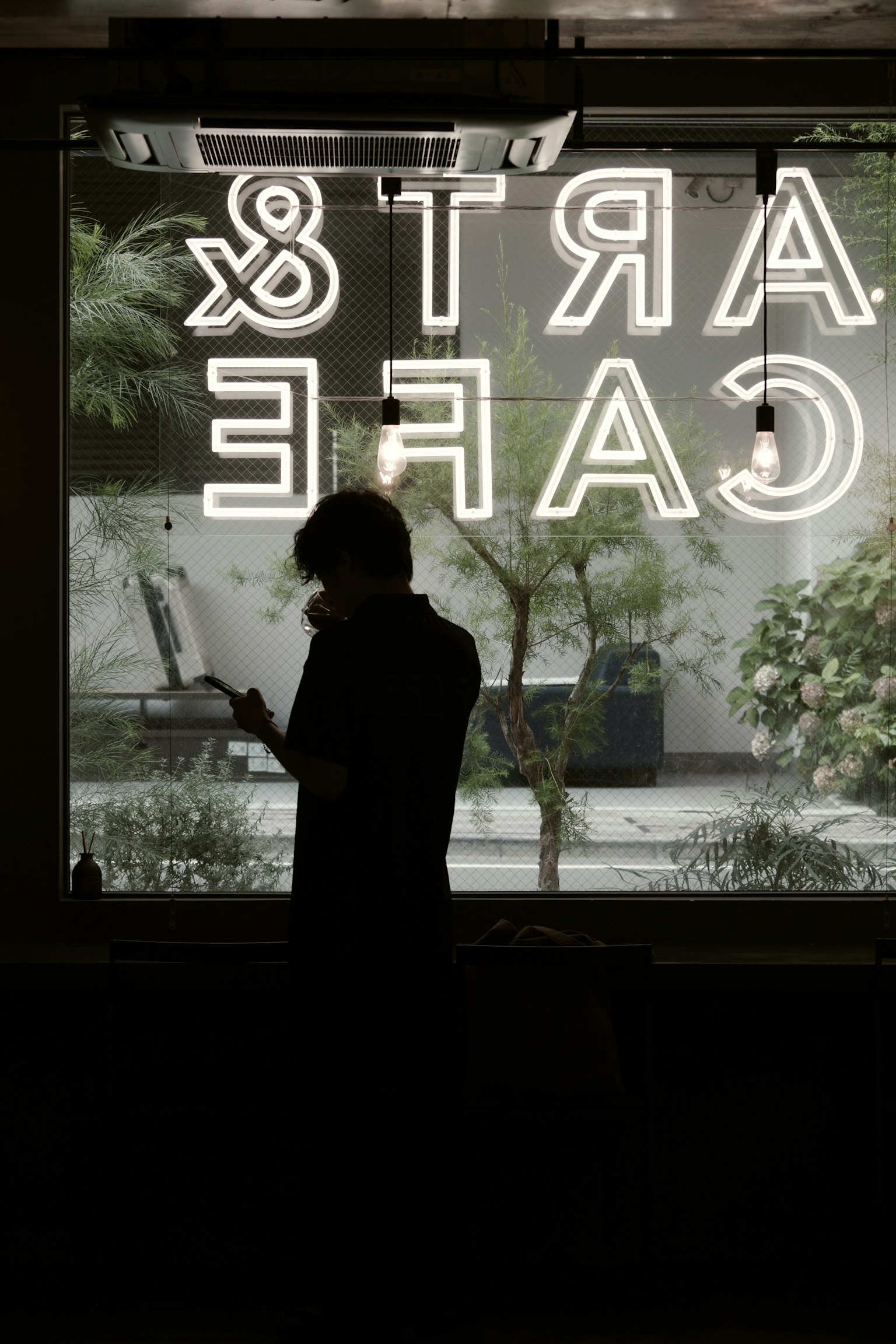 Silhouette seseorang yang berdiri di depan jendela kafe dengan tanda neon yang cerah