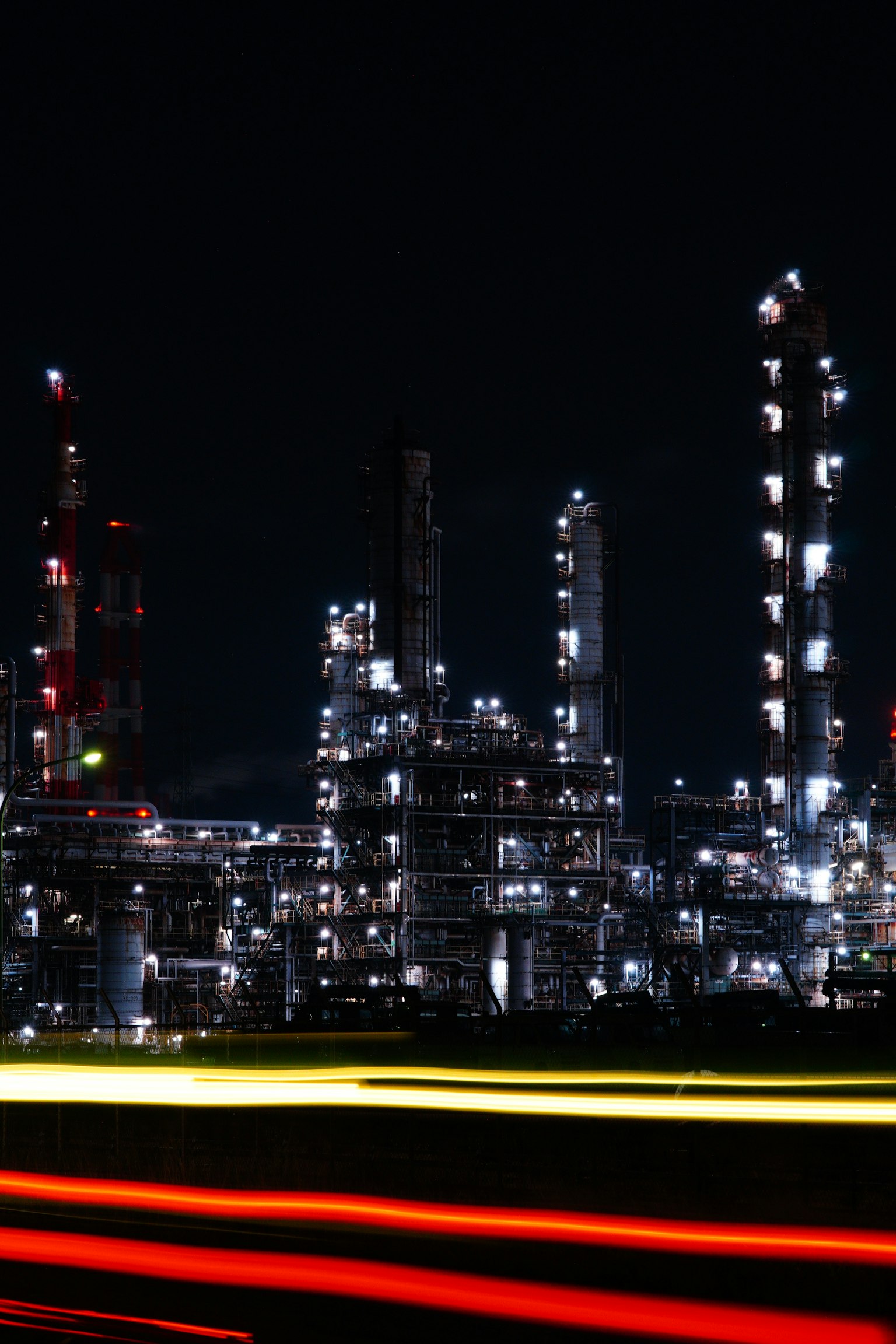 Nachtszene einer Industrieanlage mit hellen Lichtern, die Schornsteine und Tanks beleuchten