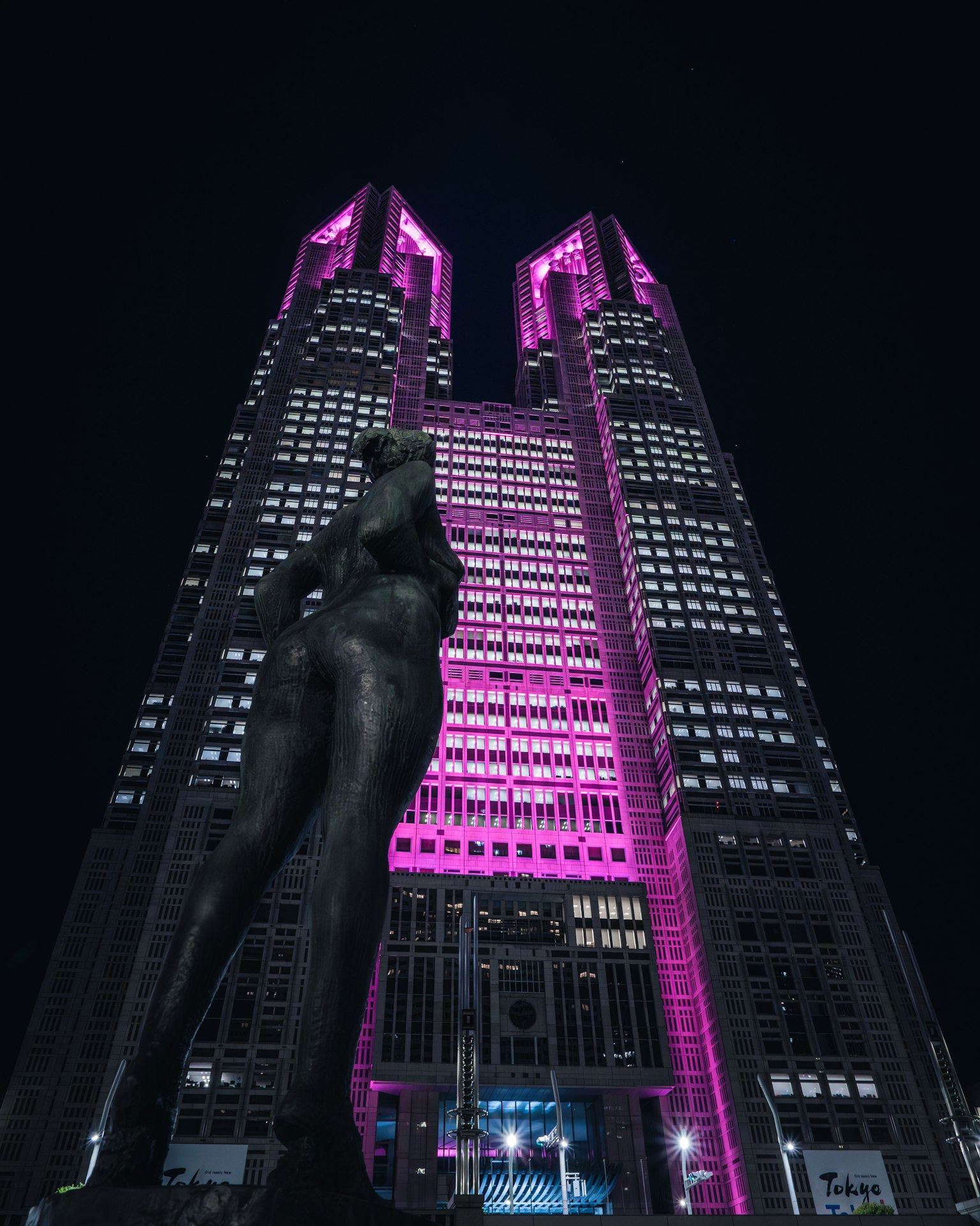 東京都政府大樓夜間粉紅色燈光照明前景中的雕像