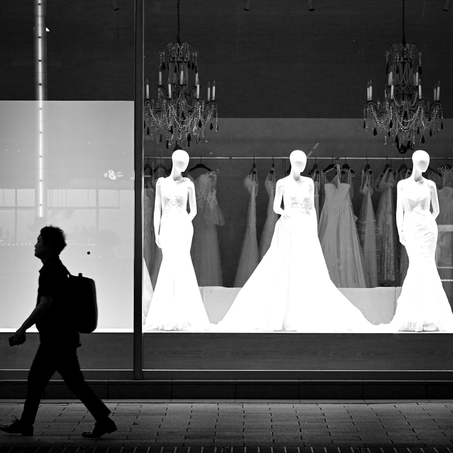 Silhouette d'une personne marchant devant une vitrine montrant des robes de mariée blanches sur des mannequins