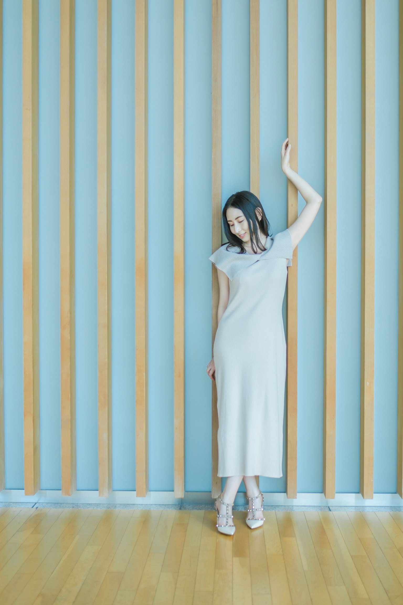 Ritratto di una donna appoggiata a un muro di legno che indossa un vestito semplice e tacchi