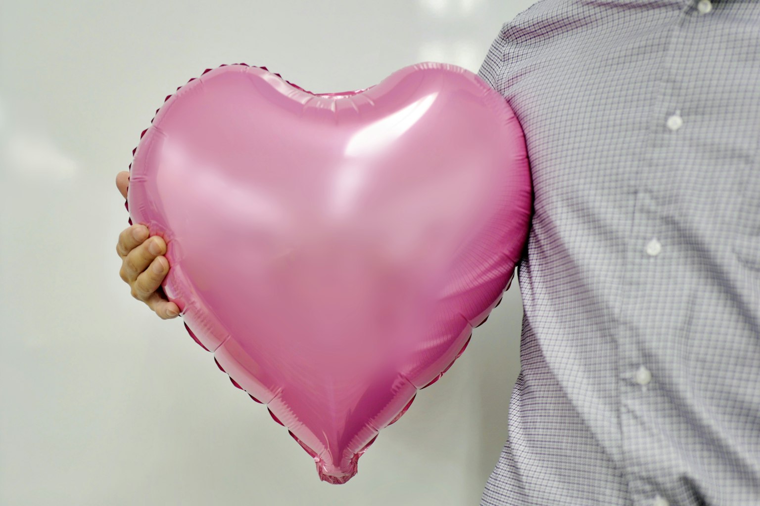 Orang yang memegang balon berbentuk hati berwarna pink