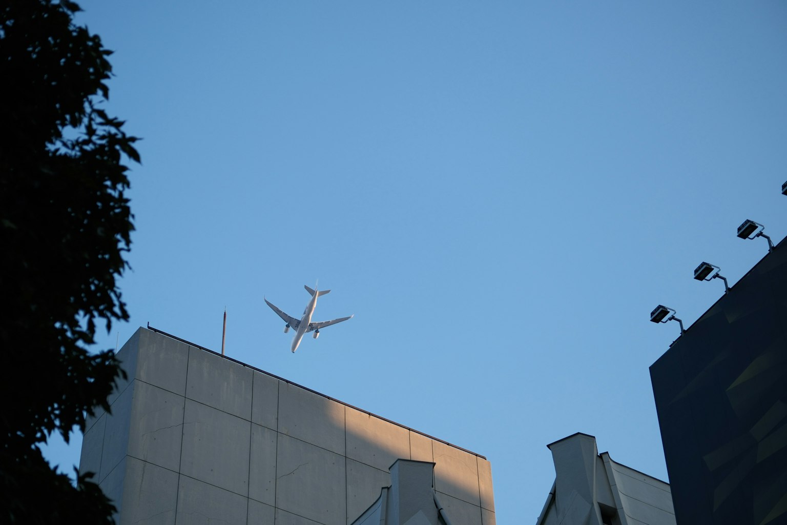 Airplane flying against a clear blue sky with building silhouettes