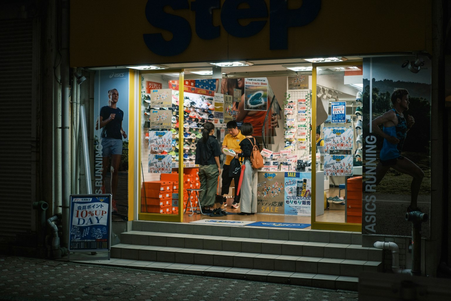Extérieur d'un magasin de sport la nuit Éclairage vif et produits exposés dans la vitrine Client et personnel à l'intérieur