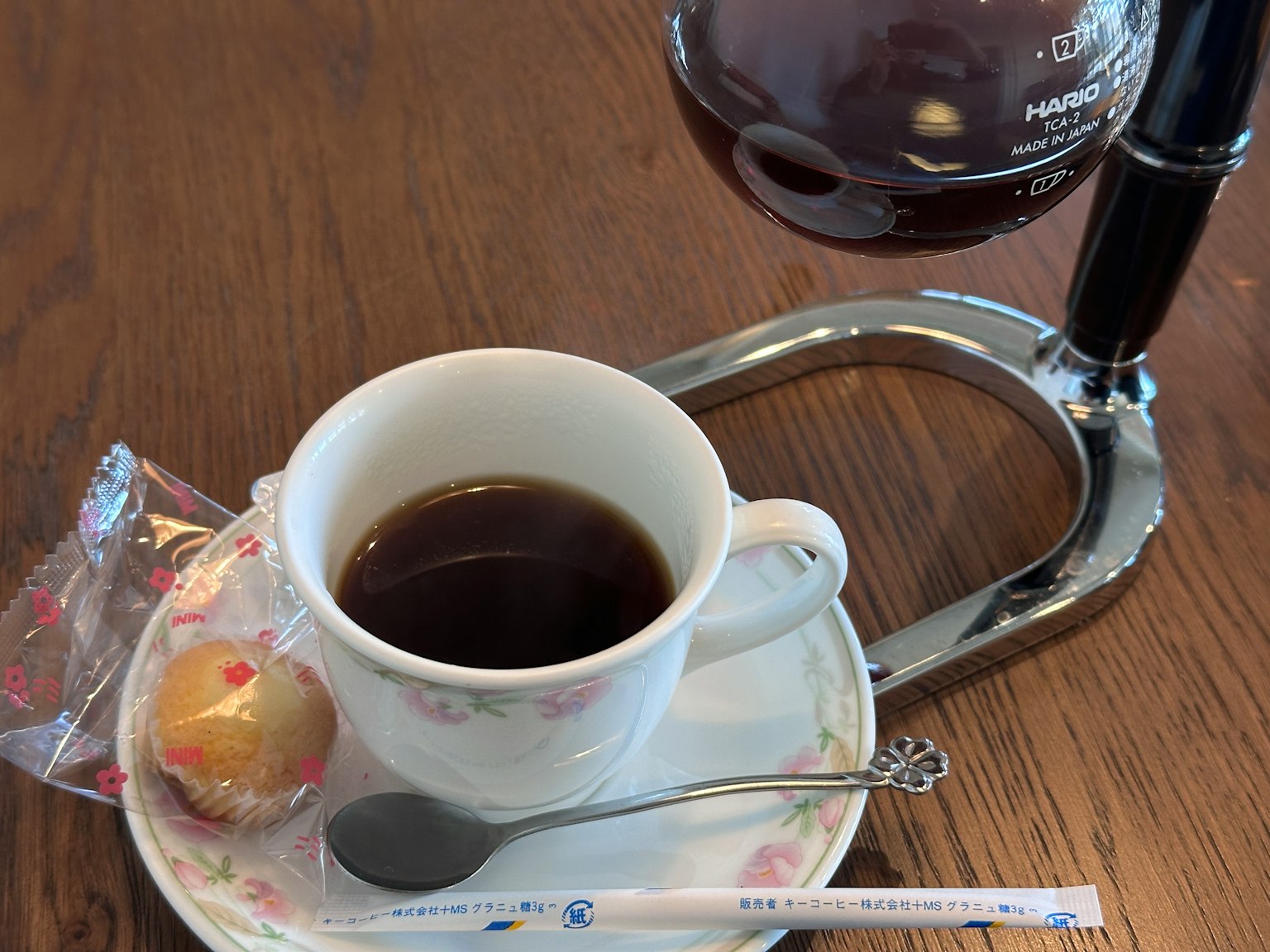 Secangkir kopi dengan camilan kecil di piring di atas meja kayu