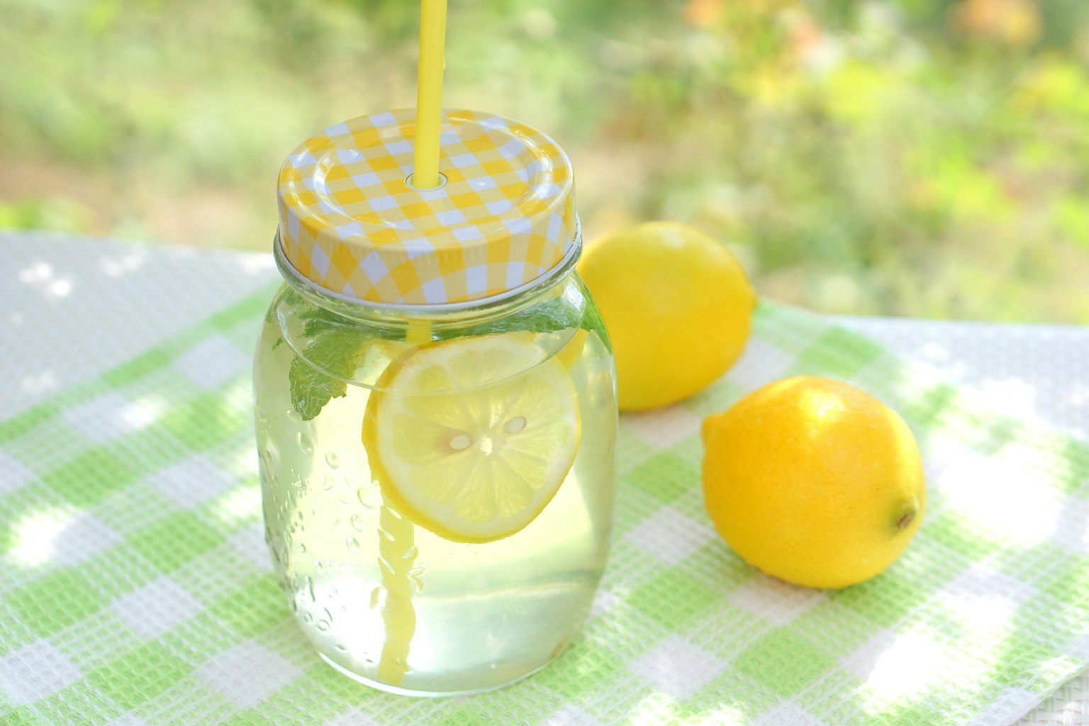 Un pot de boisson clair avec du citron et une paille à côté de citrons frais