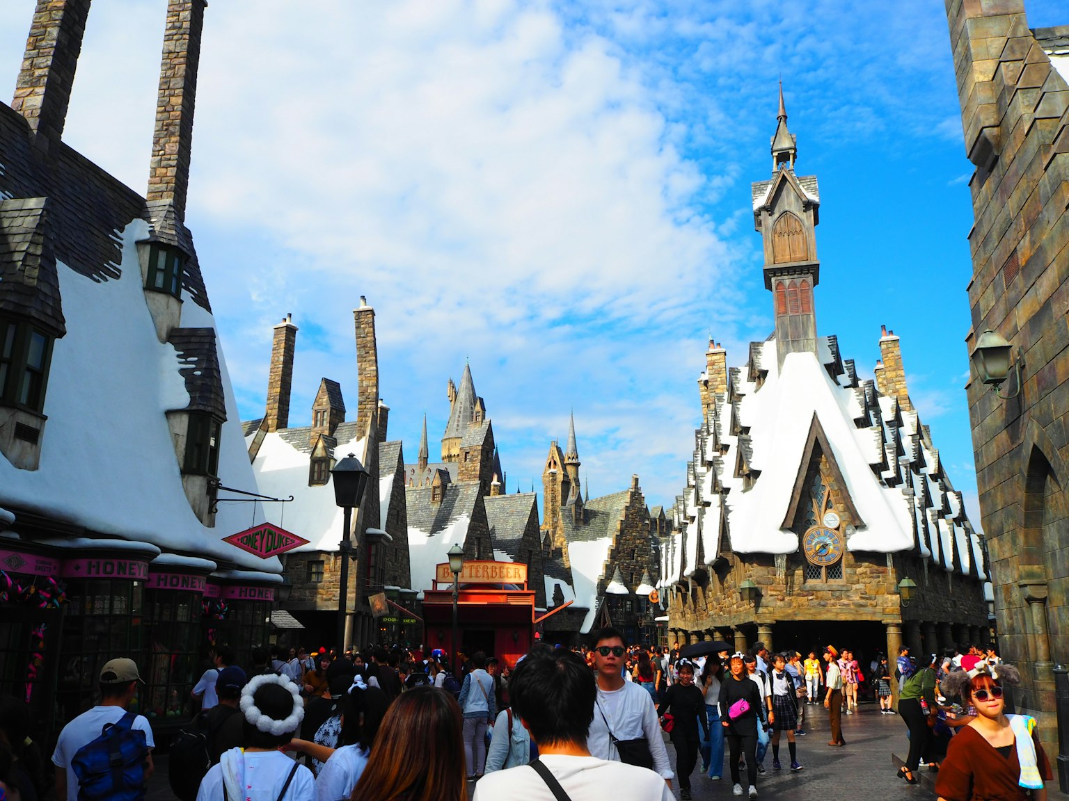 Jalan sibuk di taman bertema Harry Potter dengan bangunan indah dan langit biru