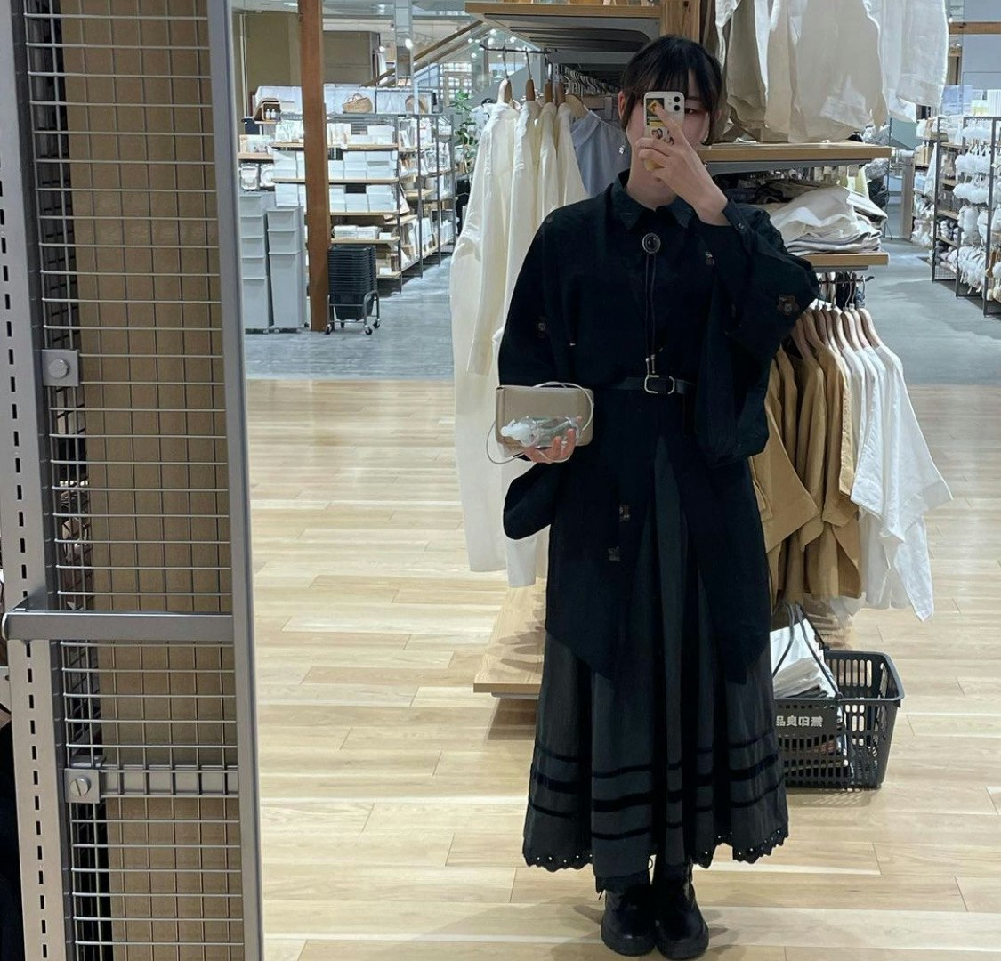 เซลฟี่กระจกของผู้หญิงที่กำลังลองใส่ฮาโอริสีดำและกระโปรงพลีทในร้านเสื้อผ้าวินเทจ