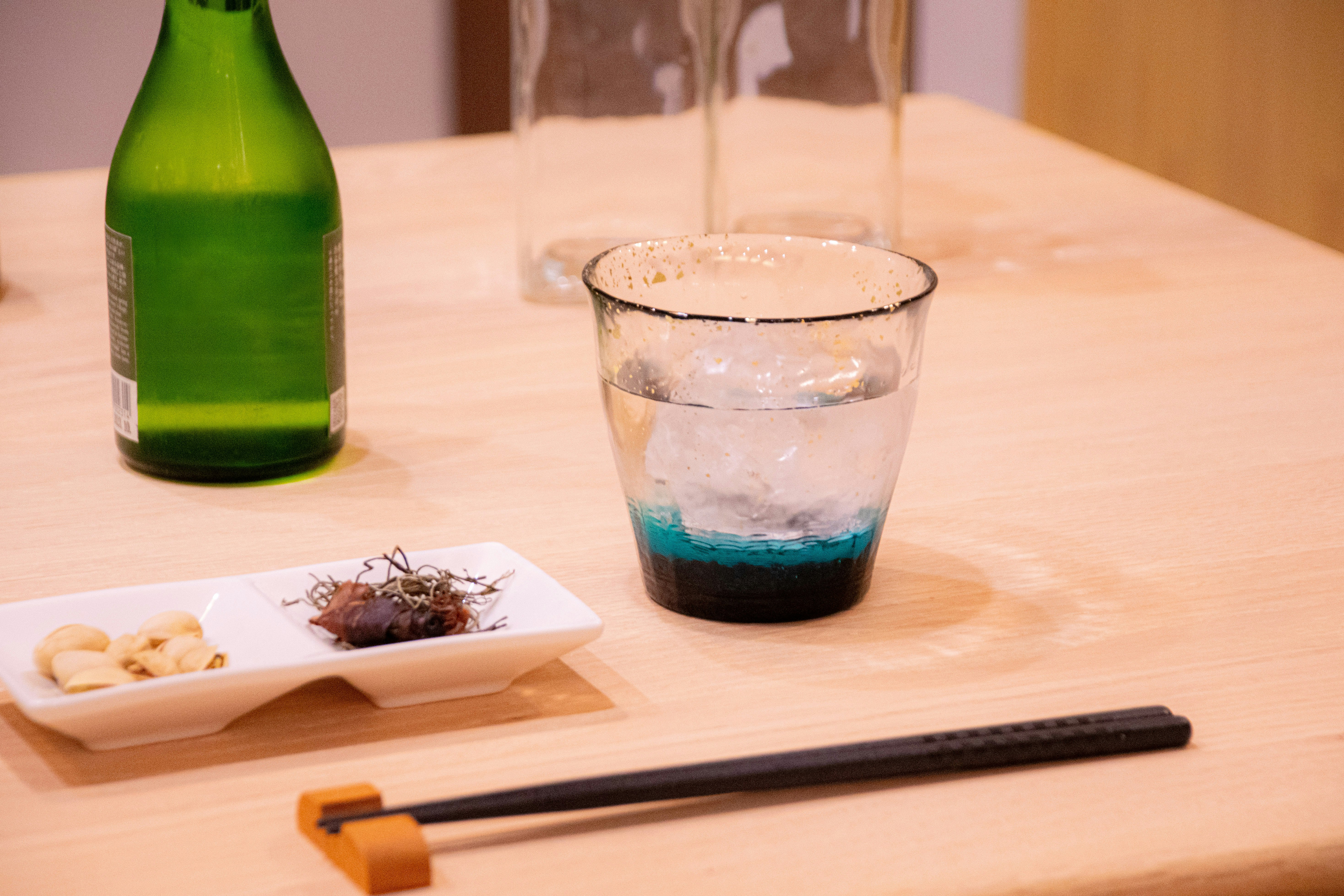绿色酒瓶、玻璃杯和筷子摆放的餐桌场景