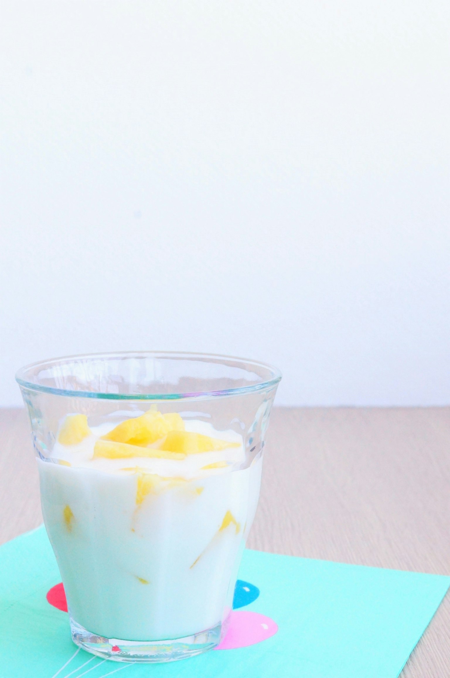 Yogurt topped with mango in a clear glass on a colorful background