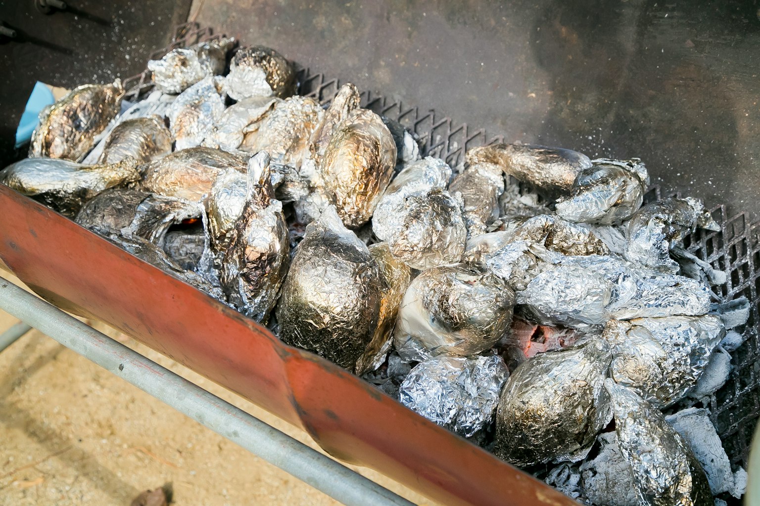 Fish heads wrapped in silver foil cooking on a grill