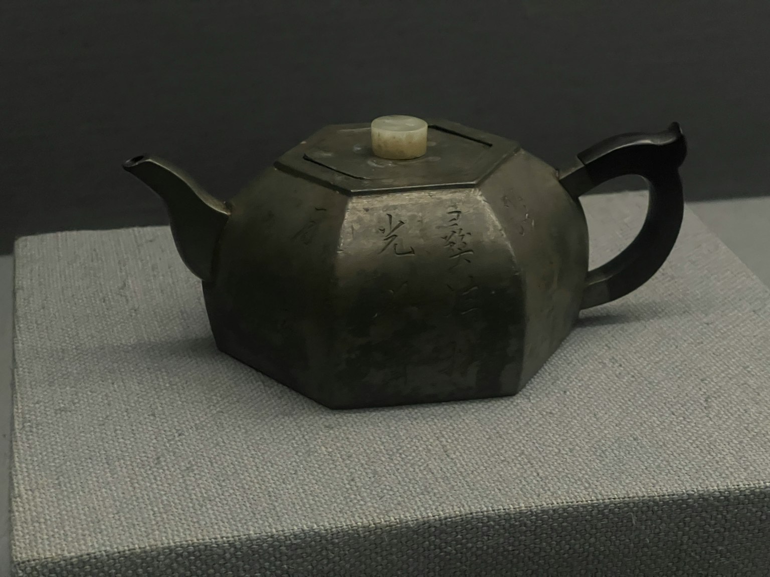 Teh pot logam heksagonal diletakkan di atas permukaan kain abu-abu