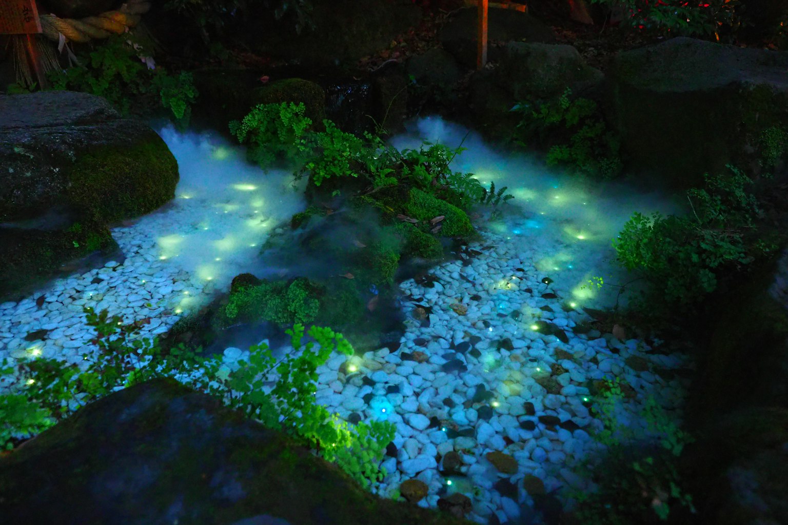 A flowing stream with glowing blue lights surrounded by stones and green plants