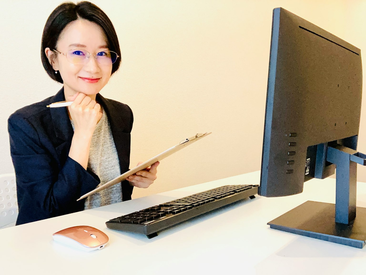 Una donna seduta a una scrivania davanti a un computer che tiene un clipboard e sorride