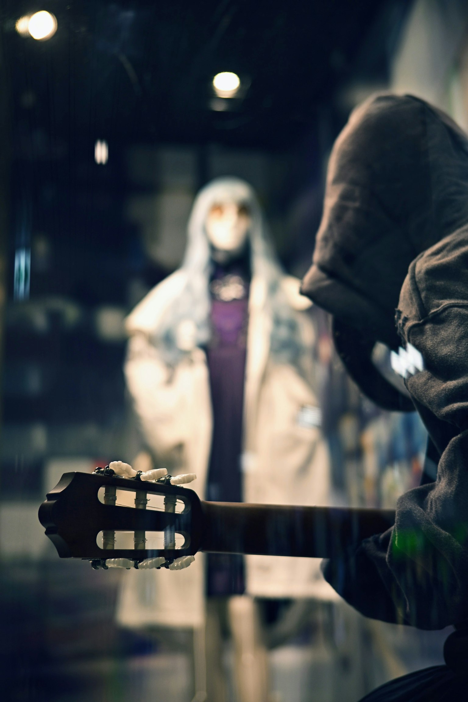 A figure holding a guitar with a mannequin dressed in a coat in the background