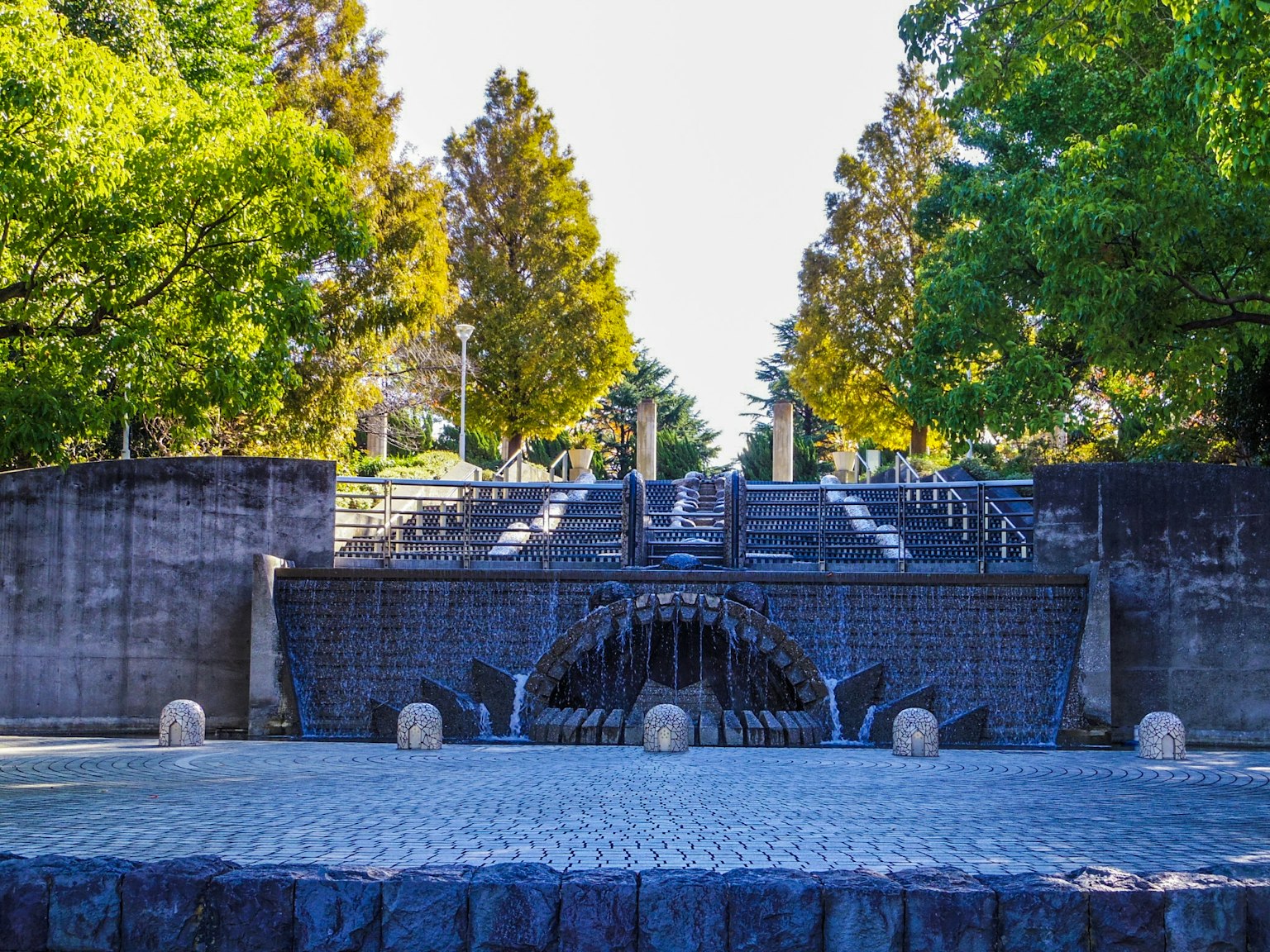 Scena di parco con fontana e scale circondate da alberi verdi vivaci e strutture in pietra