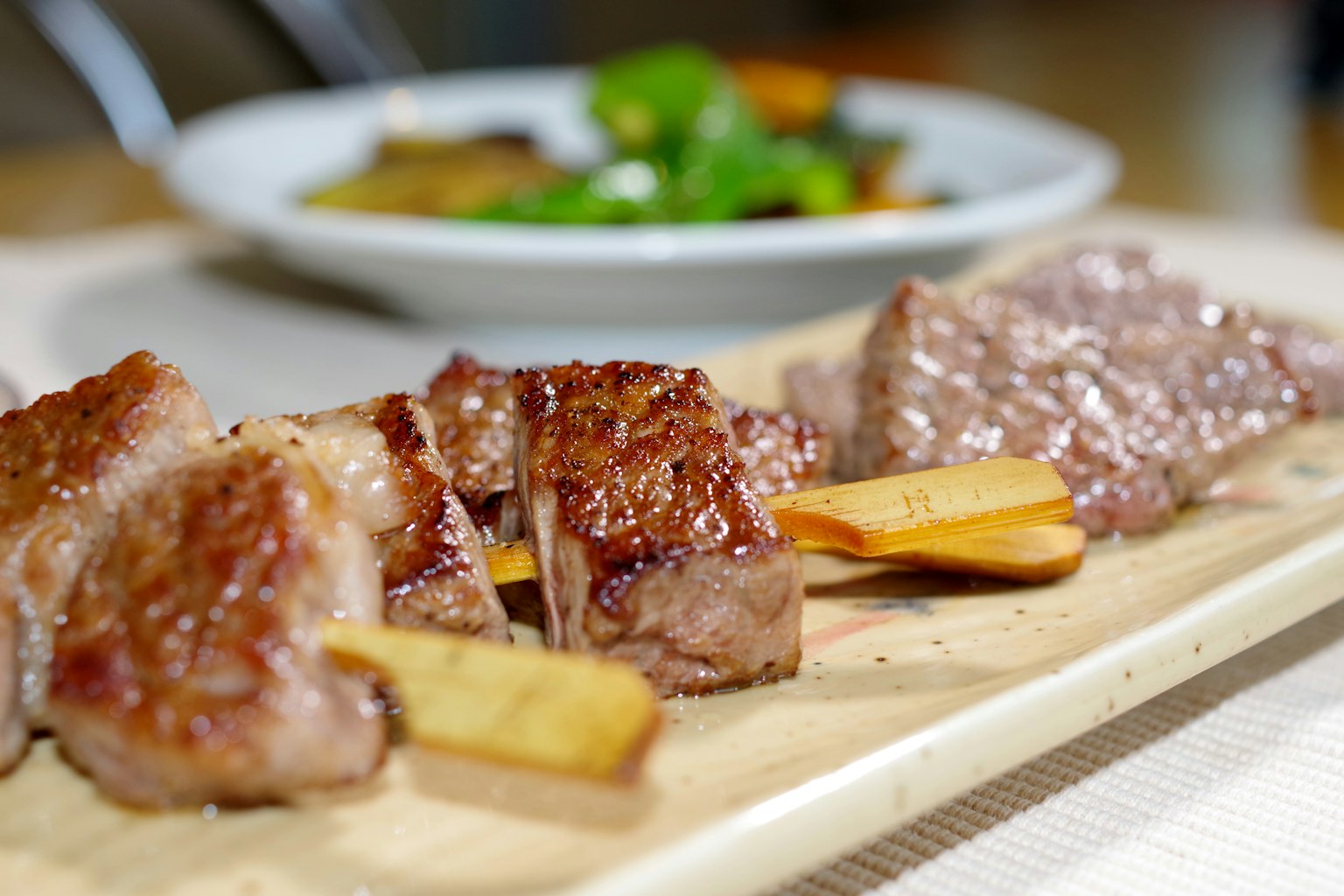 Spiedini di carne grigliata serviti su un vassoio di legno con un'insalata sullo sfondo