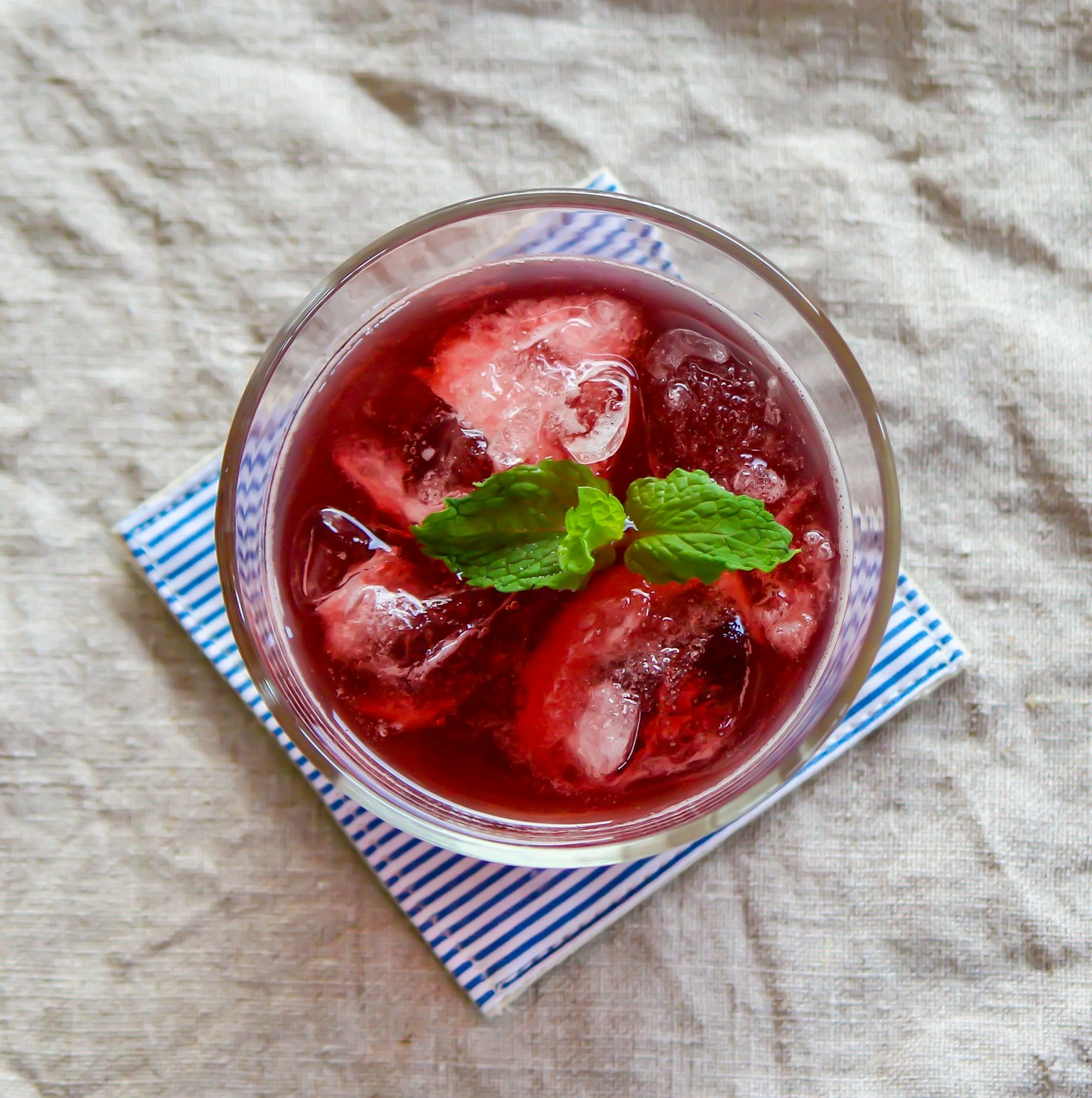 Verre de boisson rouge avec des glaçons et des feuilles de menthe sur un sous-verre rayé
