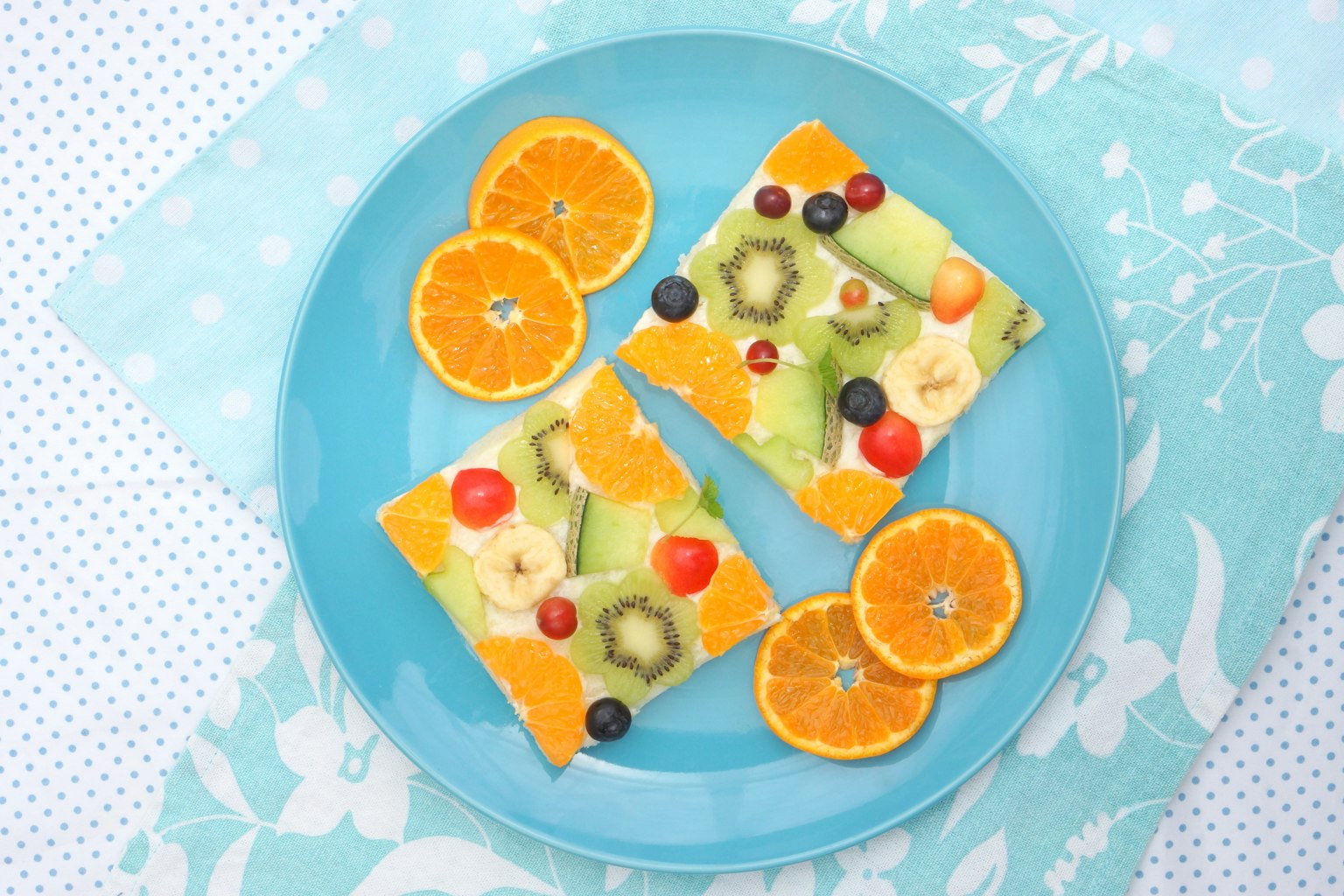 Cuadrados de gelatina de frutas cubiertos con frutas variadas en un plato azul