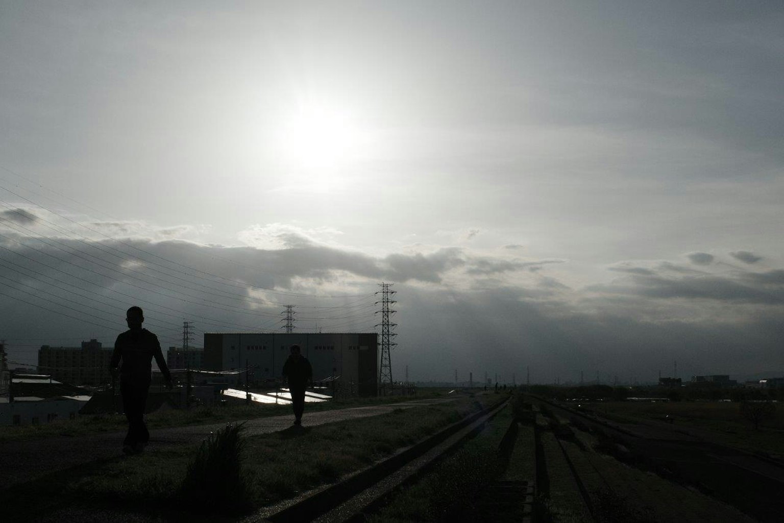 Silhouette di persone che camminano lungo una ferrovia sotto un cielo nuvoloso