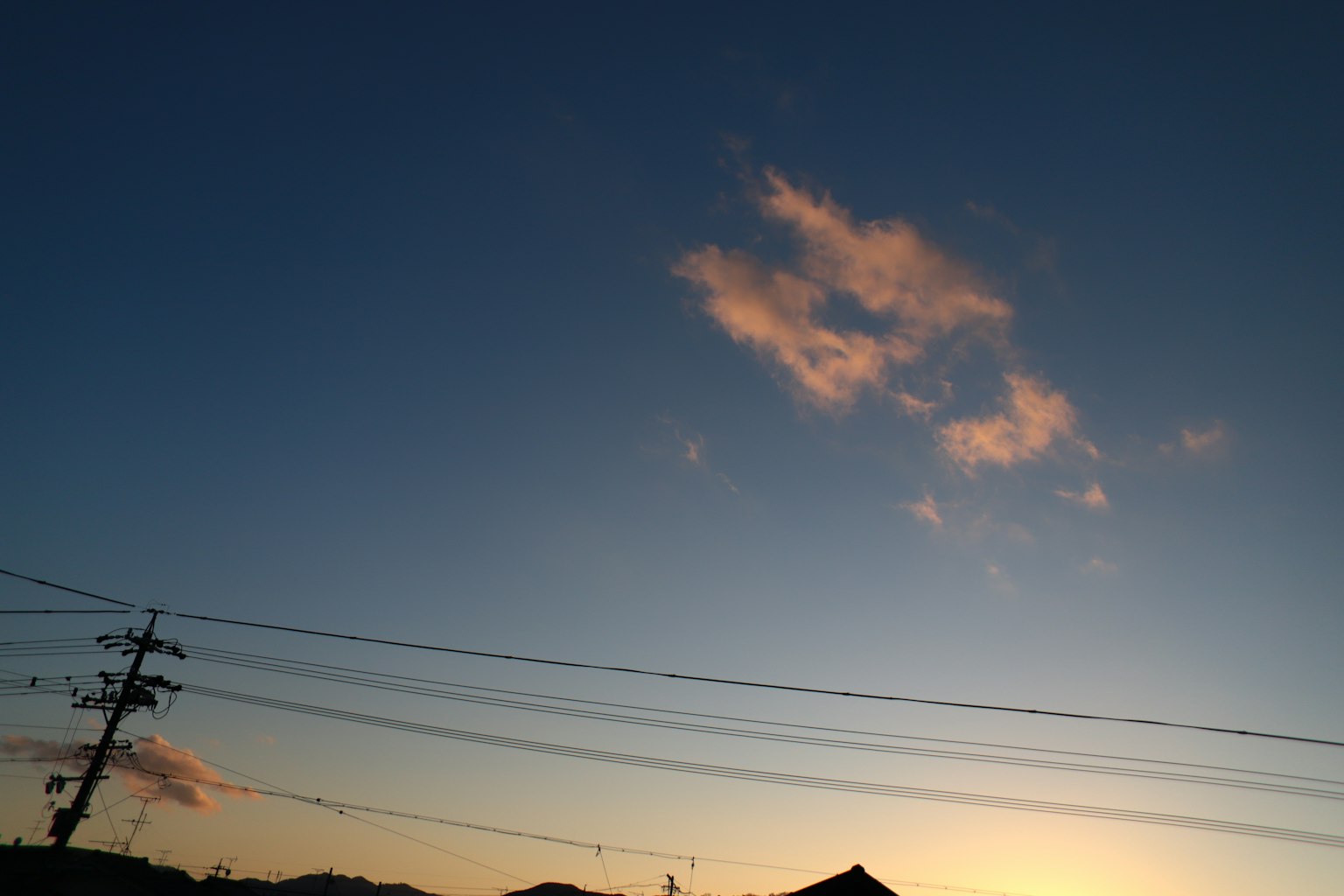 Silhouettierte Wolken gegen einen Sonnenuntergangshimmel mit Stromleitungen