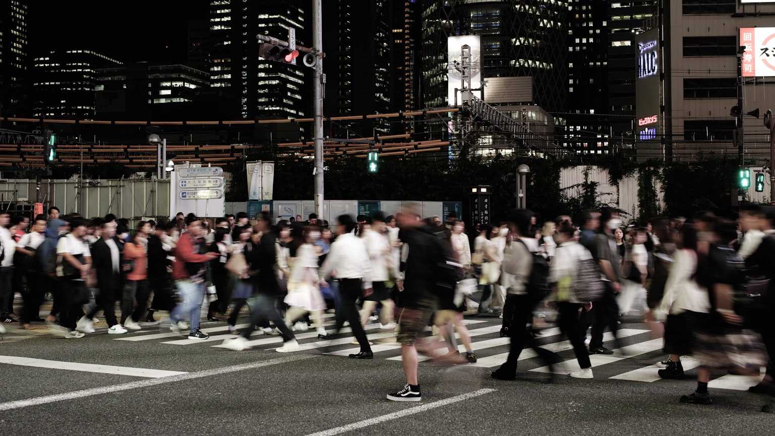 Crowd of people crossing a street at night in Tokyo with city lights in the background