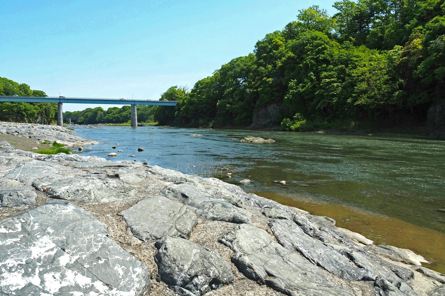 Malersicher Blick auf einen Fluss mit einer Brücke umgeben von Grün und Felsen