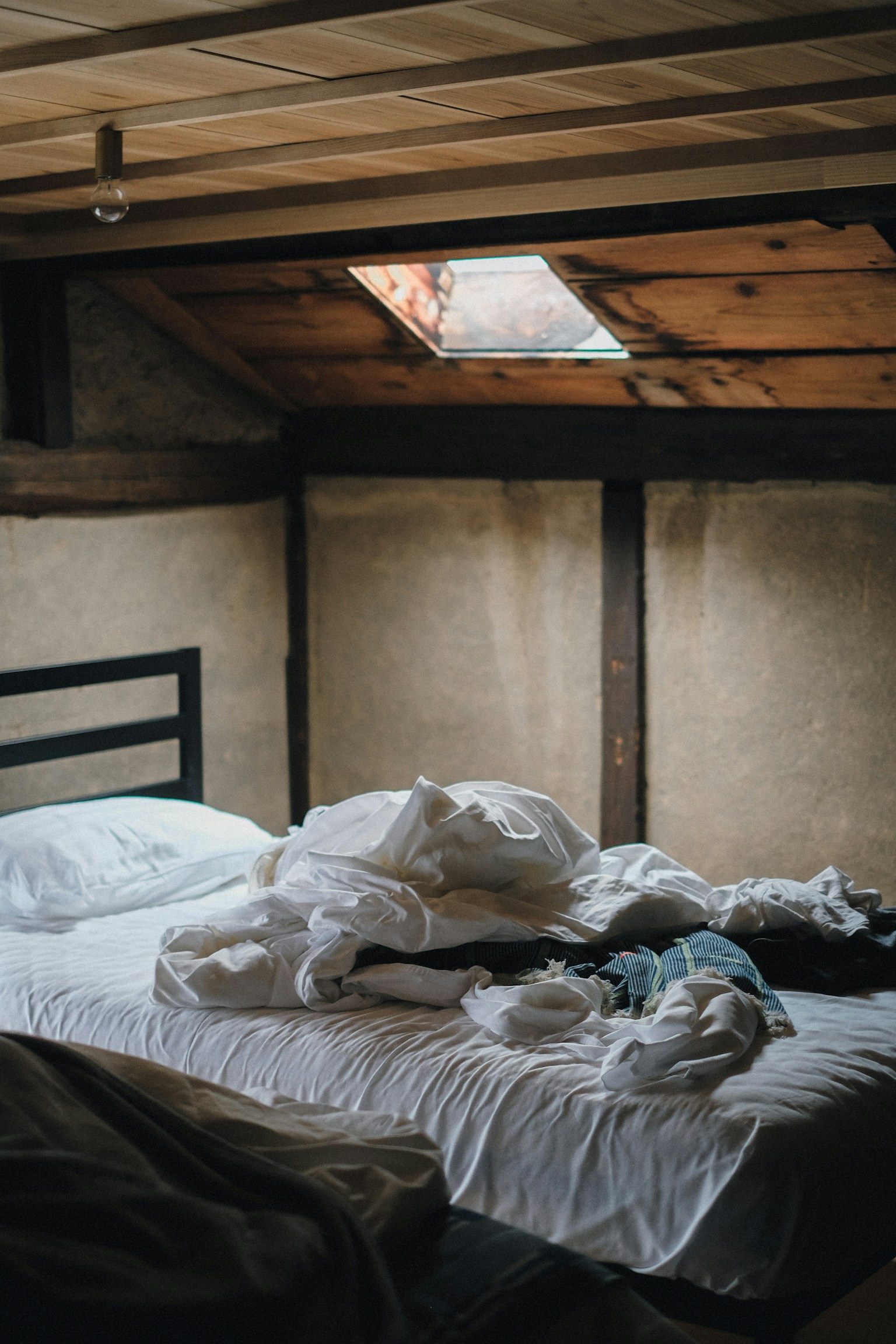 A simple bedroom interior with crumpled white sheets and blankets scattered on the bed