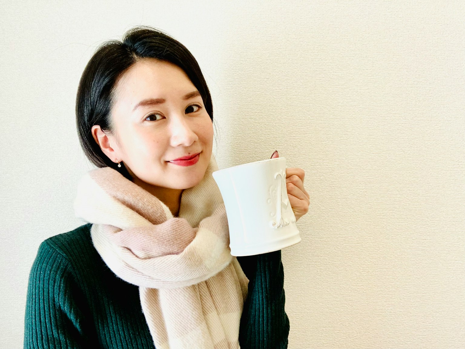 一位穿著圍巾的女性微笑著舉著白色的杯子