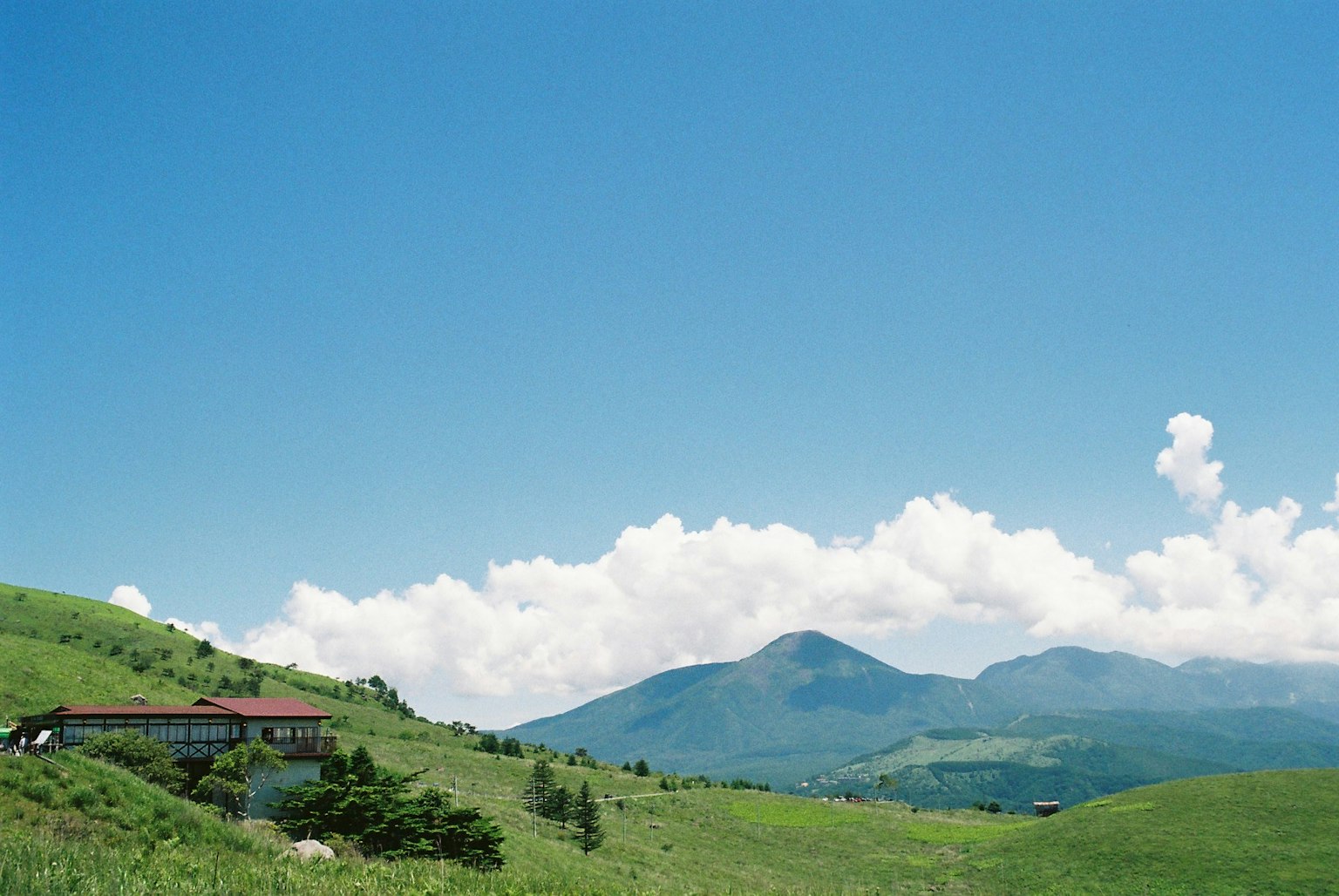 Green hills and mountains under a blue sky with white clouds