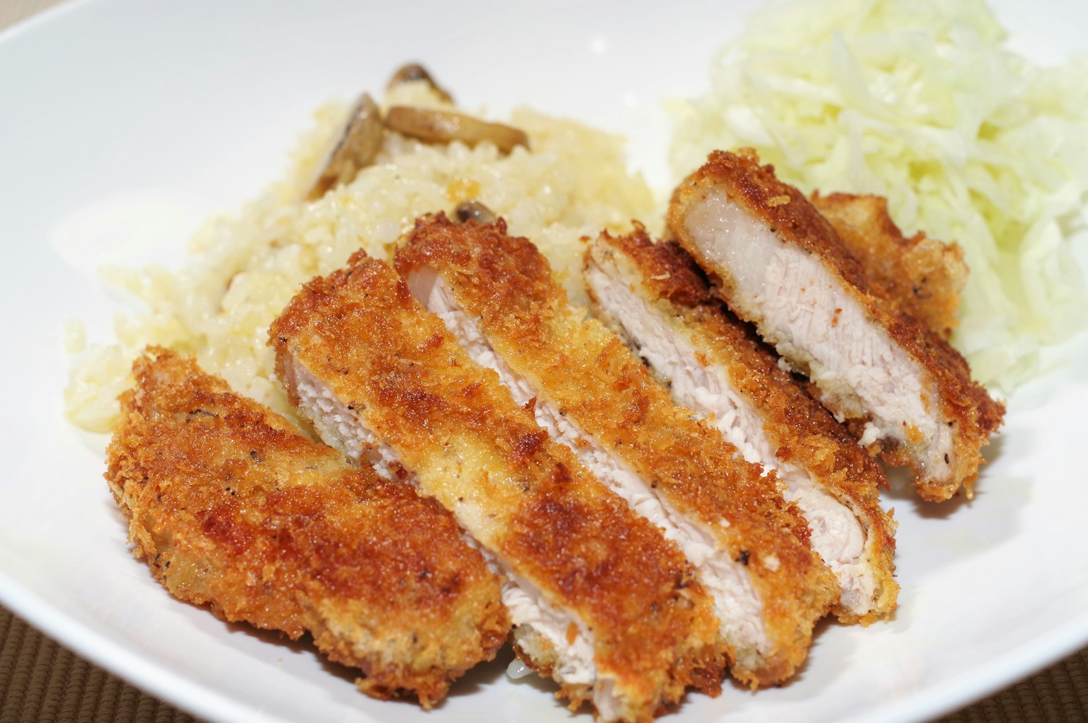 In Scheiben geschnittenes paniertes Schweinekotelett, serviert mit Reis und gehobeltem Kohl