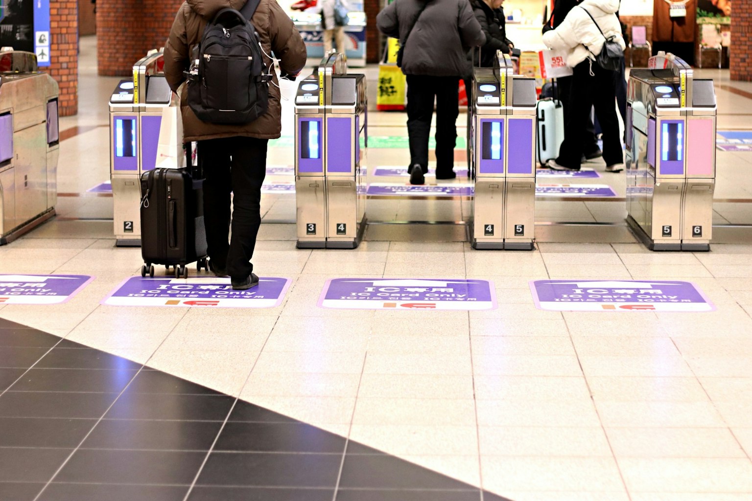 Passeggeri che passano attraverso un tornello della stazione con un viaggiatore con una valigia
