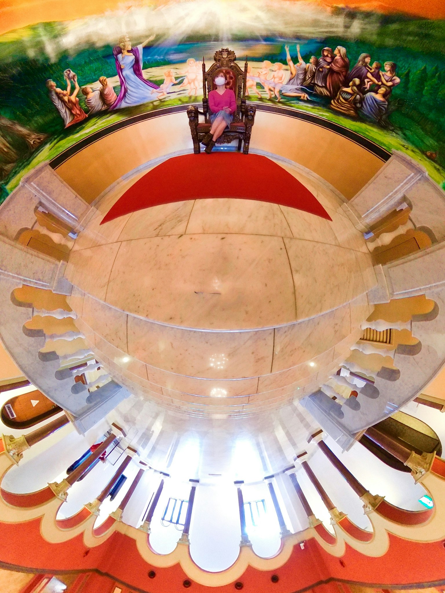 Panoramablick auf einen Raum mit einer sitzenden Figur auf einem Thron und bunten Wandmalereien