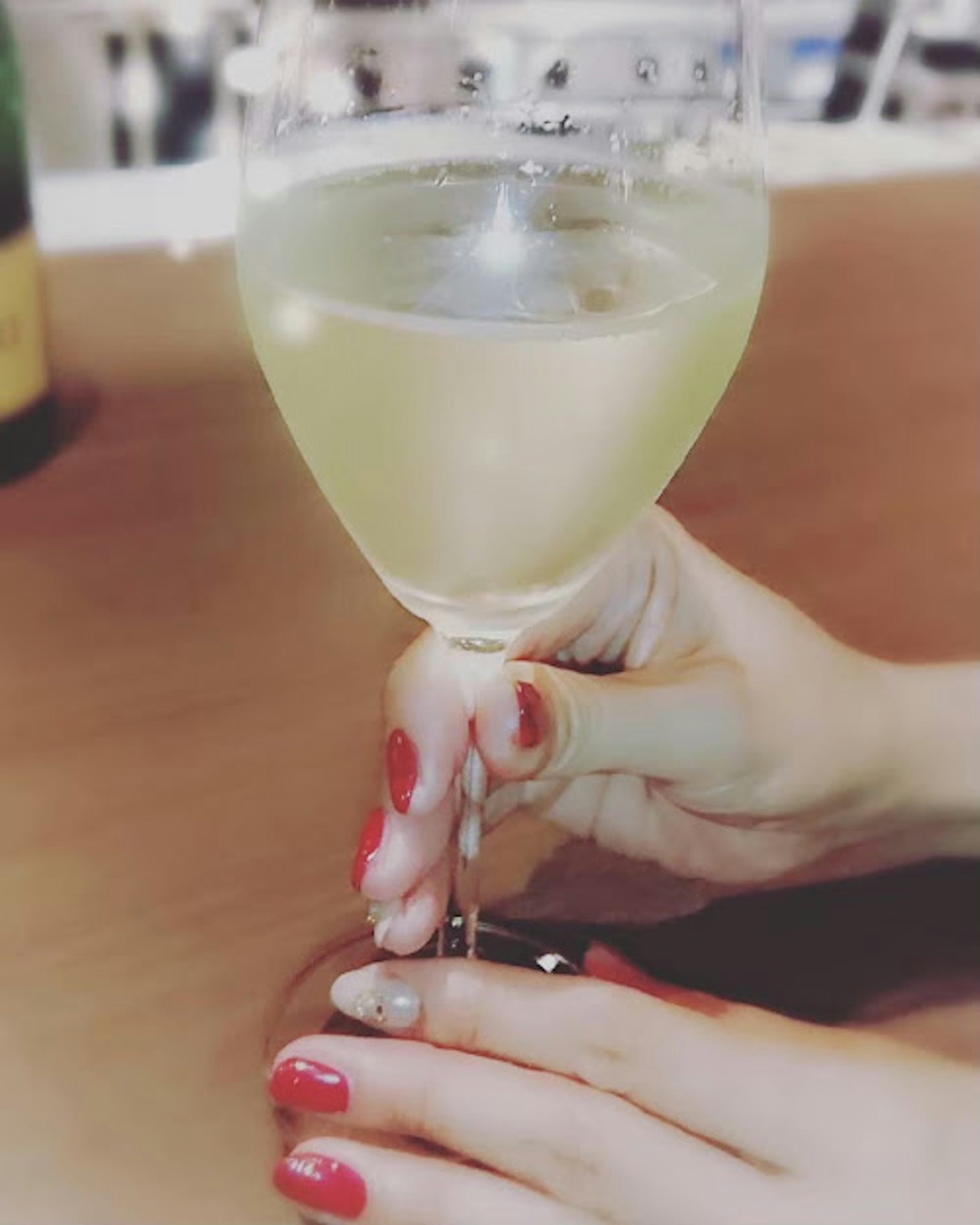 Mano sosteniendo una copa de vino blanco con uñas rojas