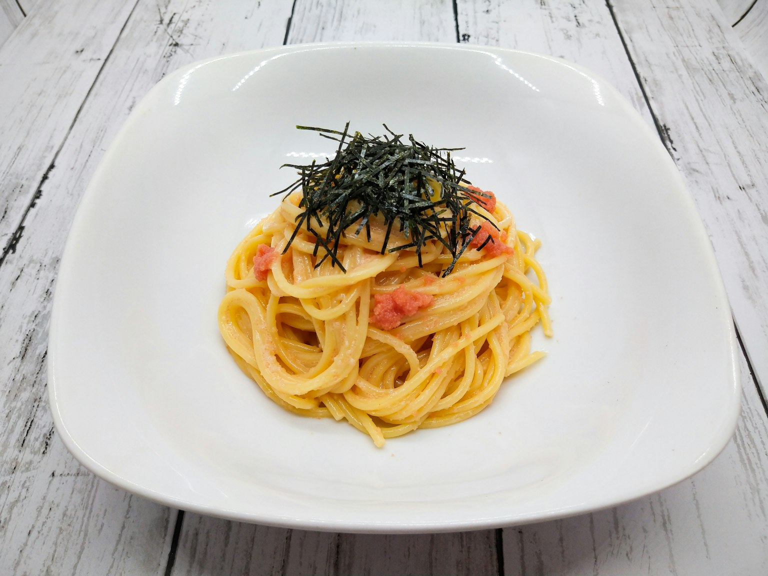 Creamy pasta topped with seaweed on a white plate
